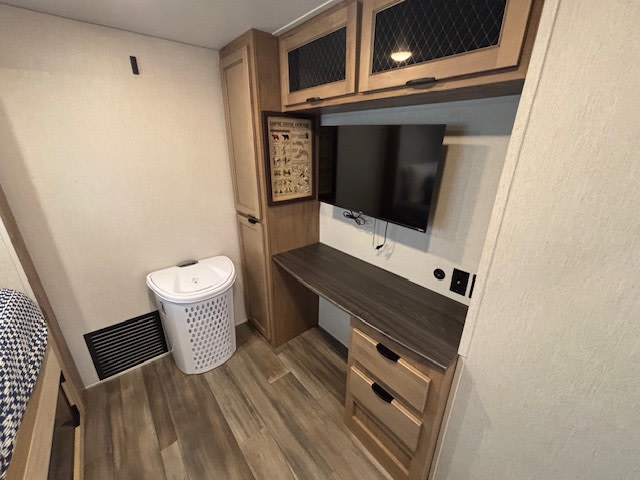 RV rental's compact desk area with TV, cabinets, and laundry hamper, ideal for productivity & comfort.. Forest River Sabre 2024