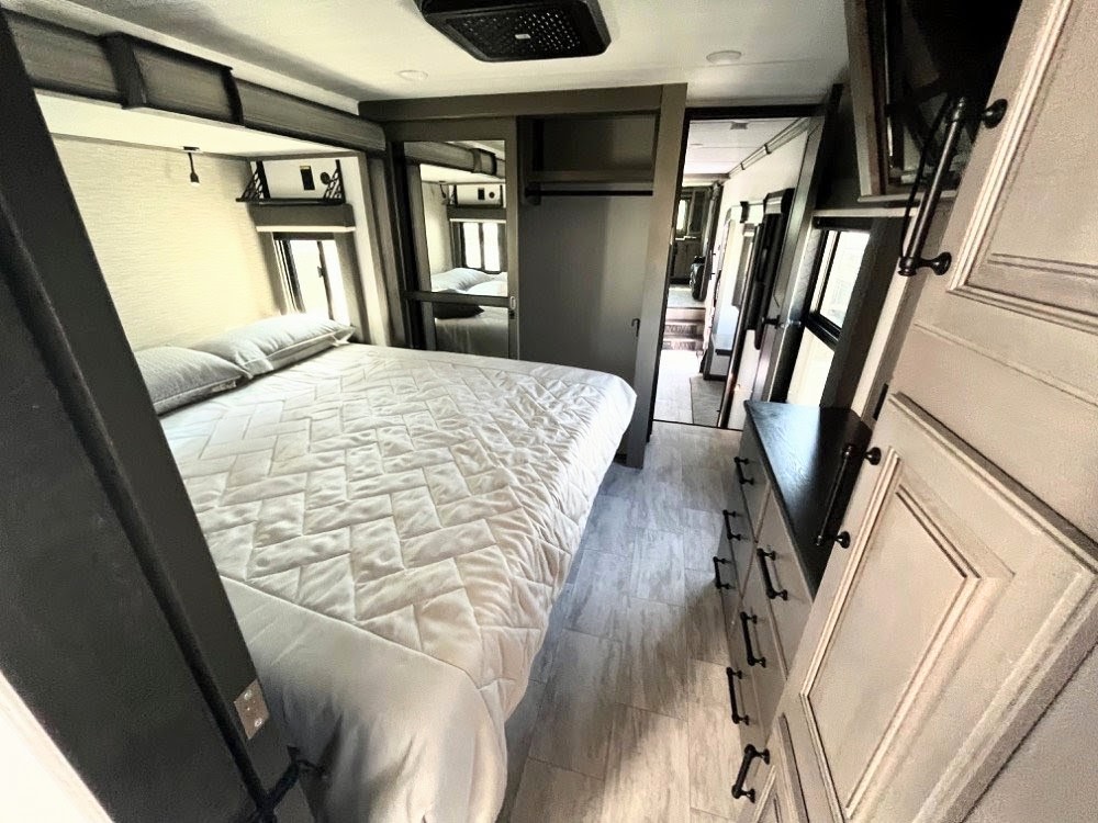 Modern RV rental bedroom featuring a large bed, dresser, and overhead storage, offering comfortable travel.. Keystone RV Montana Legacy 3761 FL 2023