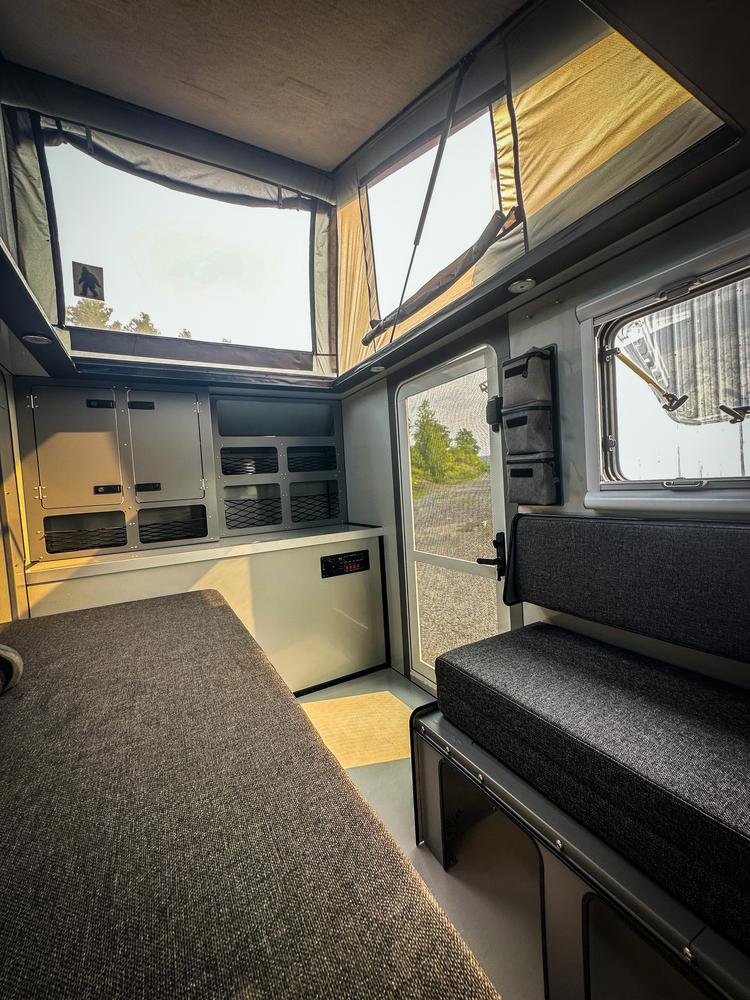 RV rental interior: A modern camper with a bed, bench, storage, and open pop-top windows revealing panoramic outdoor views.. Epik Scout 2024
