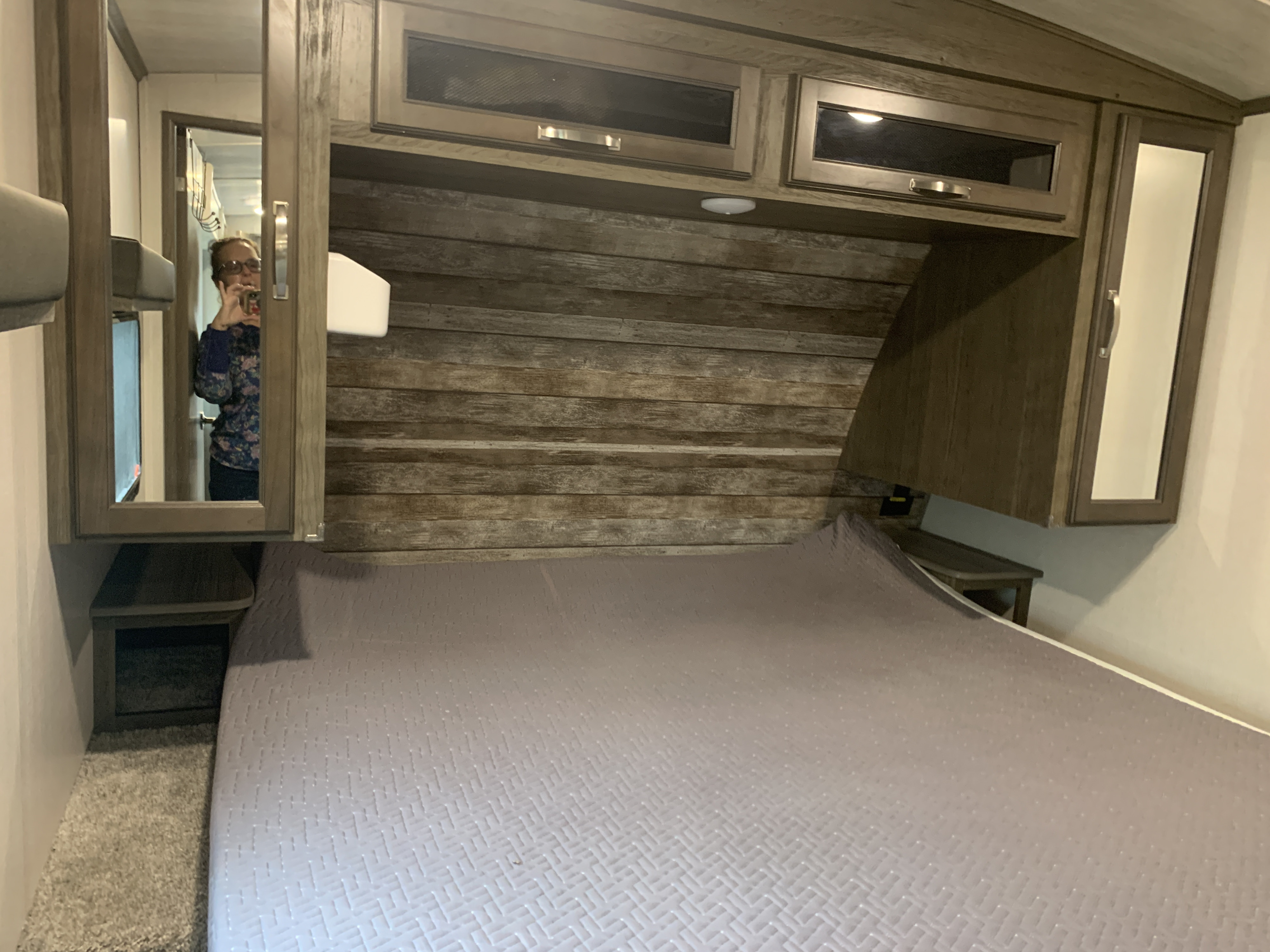 Cozy RV rental bedroom featuring a queen bed with a quilted spread, wood plank headboard, and mirrored overhead cabinets.. Keystone RV Cougar 2023