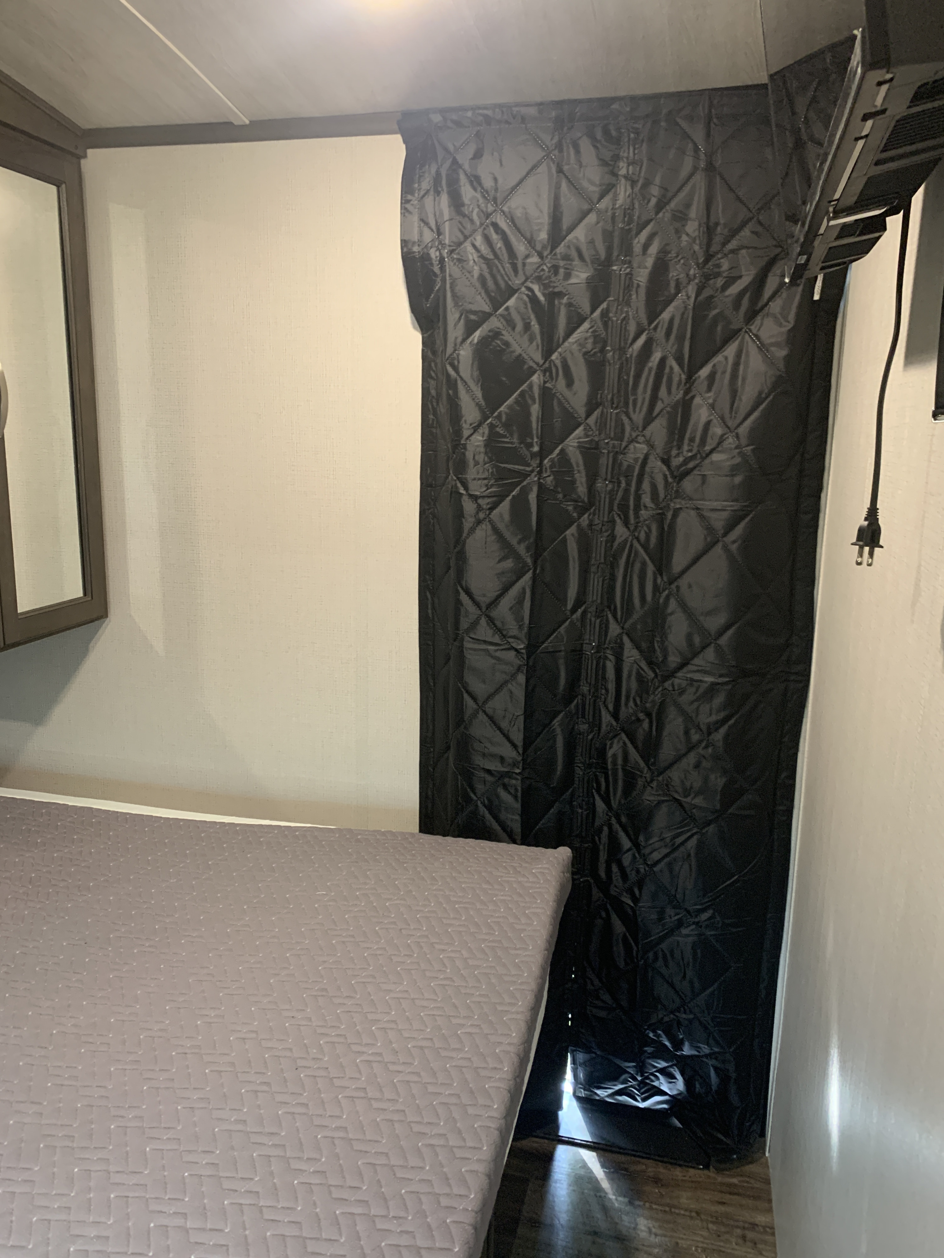 RV rental interior featuring a bed with grey mattress, a black quilted privacy curtain, and a wall-mounted appliance.. Keystone RV Cougar 2023