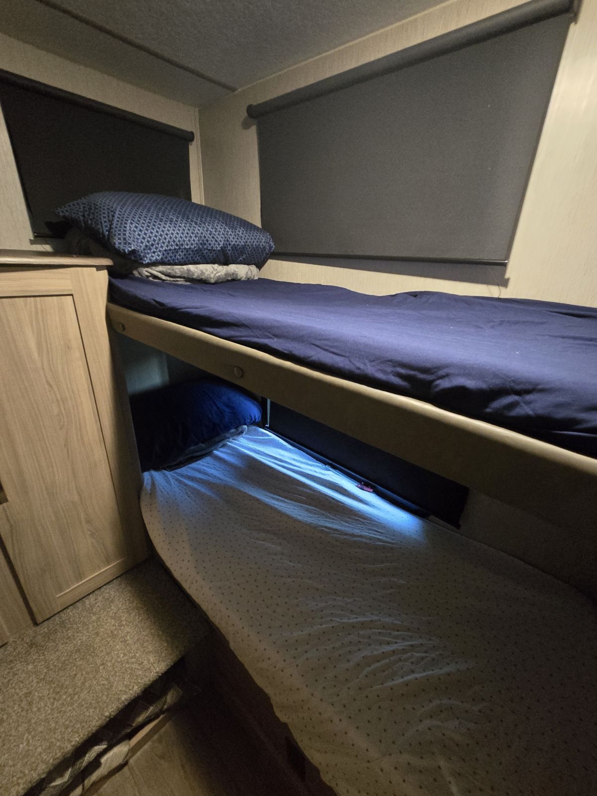 Cozy bunk beds in an RV rental, featuring navy sheets on top, a patterned sheet below, and dark window blinds.. Coachmen Freedom Express Liberty Edition 292BHDSLE 2021