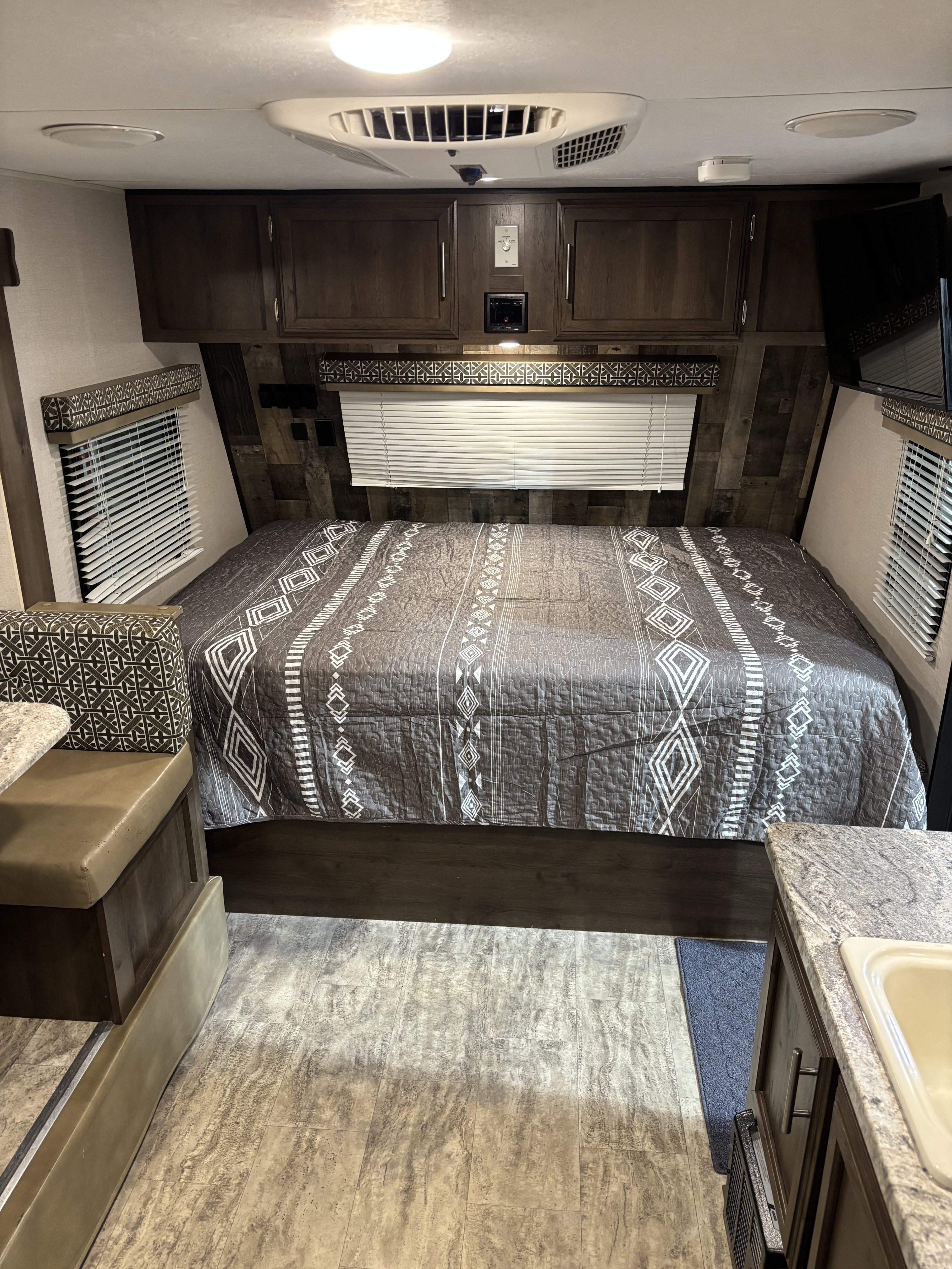 Cozy RV rental interior: patterned bed, overhead cabinets, AC, TV, and dinette with kitchenette for comfortable travel.. KZ Escape 2018