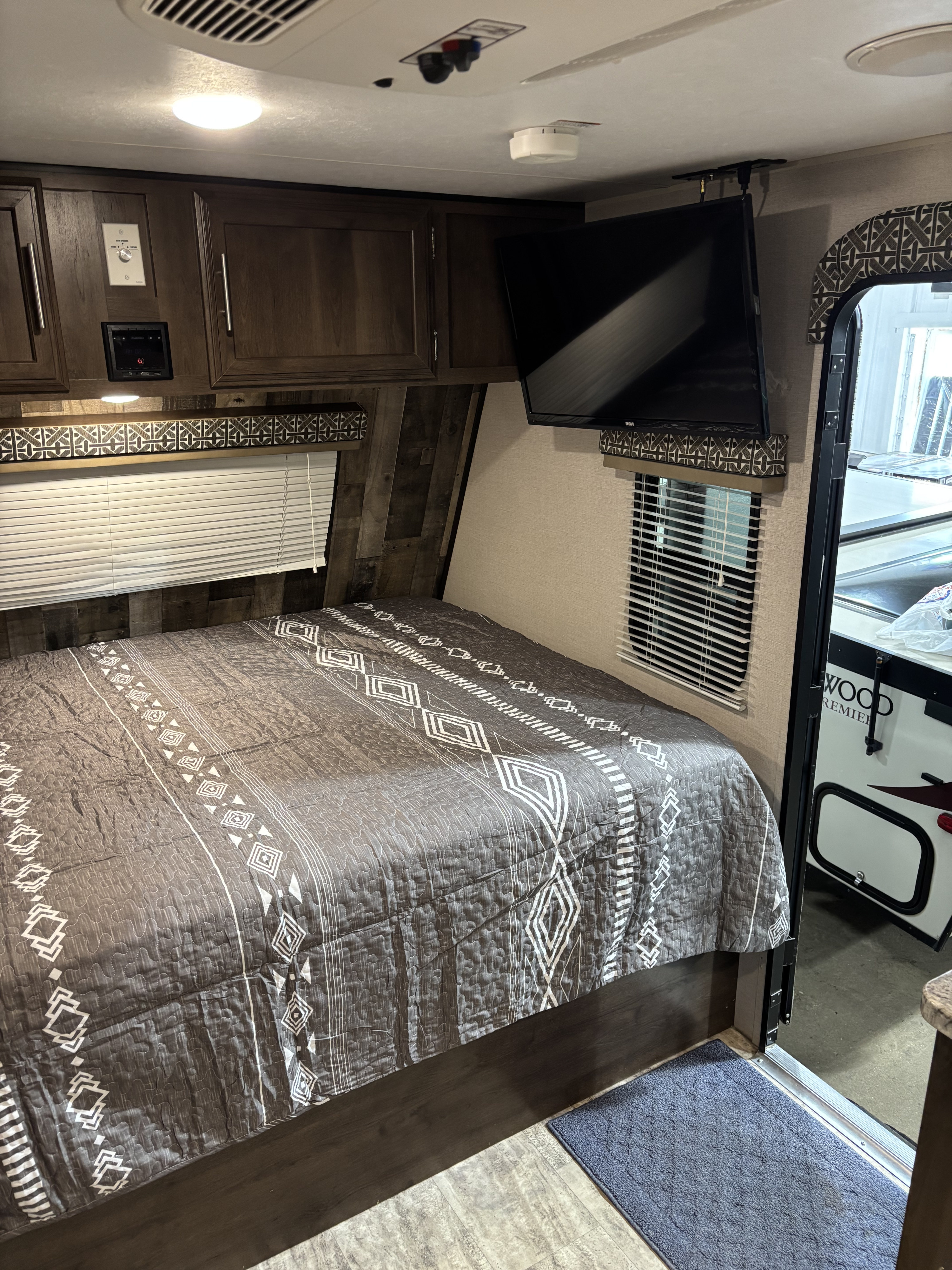 Cozy RV rental bedroom with patterned bed, wall-mounted TV, cabinets, and ceiling controls for comfortable travel.. KZ Escape 2018