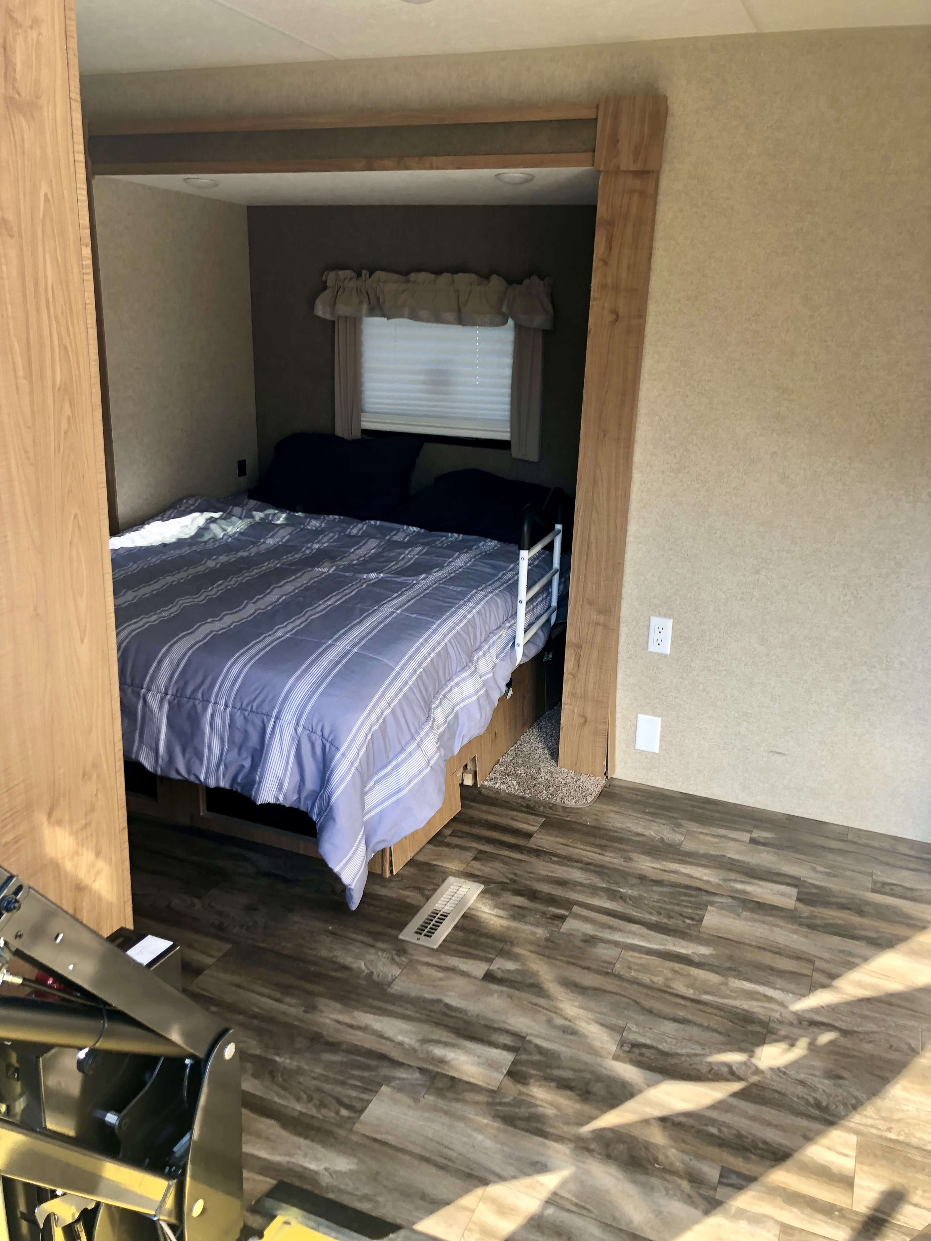 This RV rental's bedroom offers a cozy space with a bed, striped bedding, pillows, and a window. Wood-look floor and panels are visible.. HL Enterprise Unknown 2020