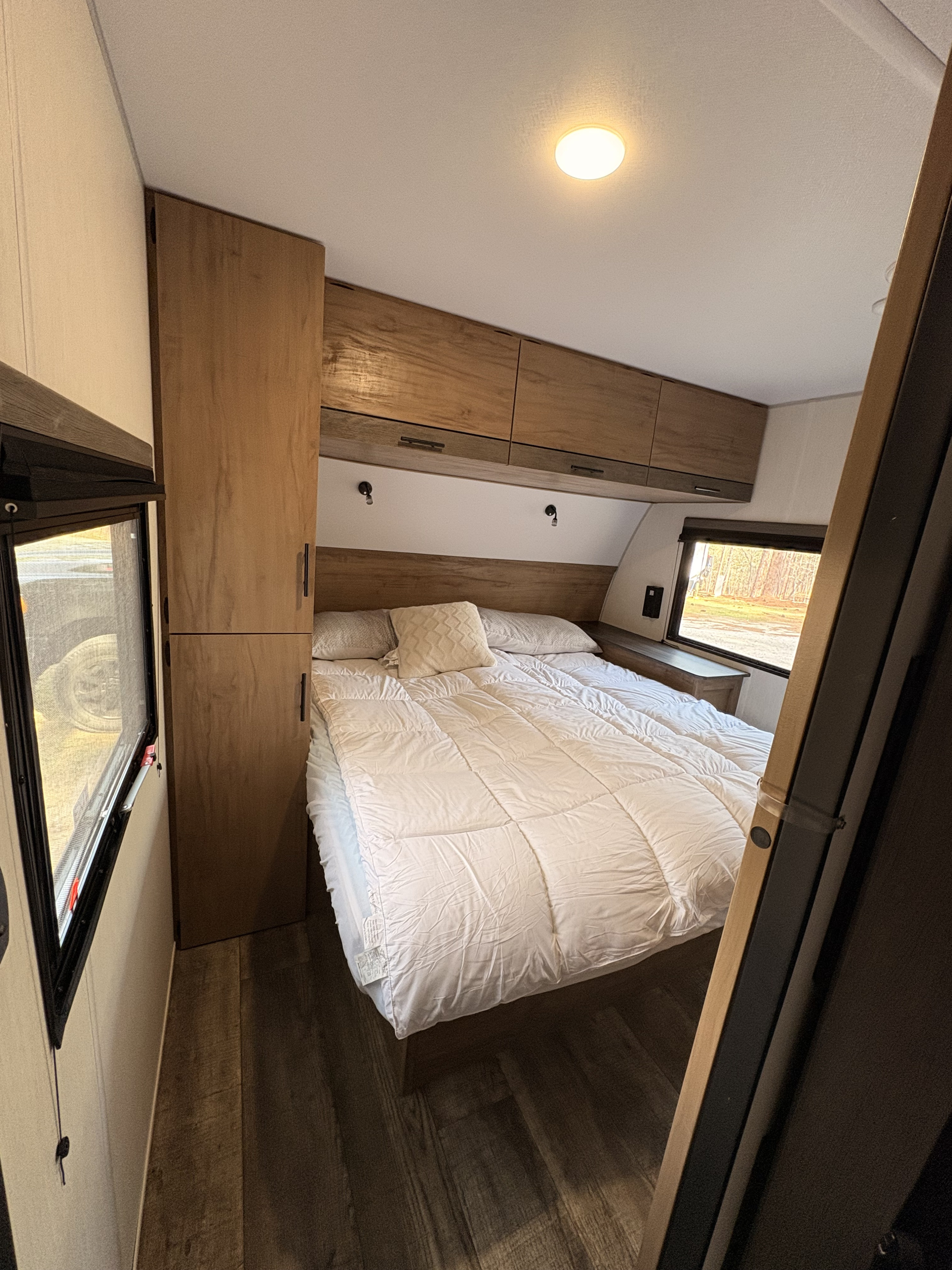 Experience comfortable travel in this RV rental bedroom, featuring a cozy bed, white bedding, and smart wooden storage.. Forest River Campsite Reserve 2024