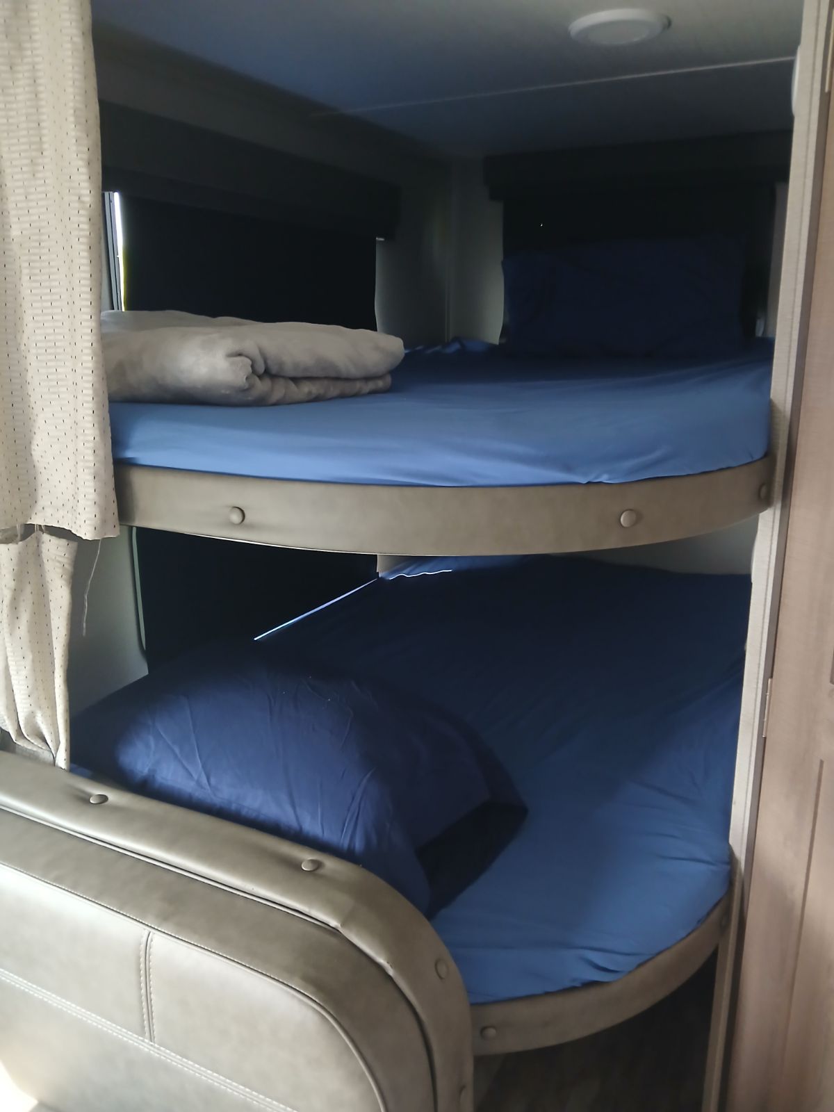 Cozy RV rental interior with two bunk beds, complete with blue sheets and pillows, a grey blanket on the top bunk.. Grand Design Imagine XLS 2022