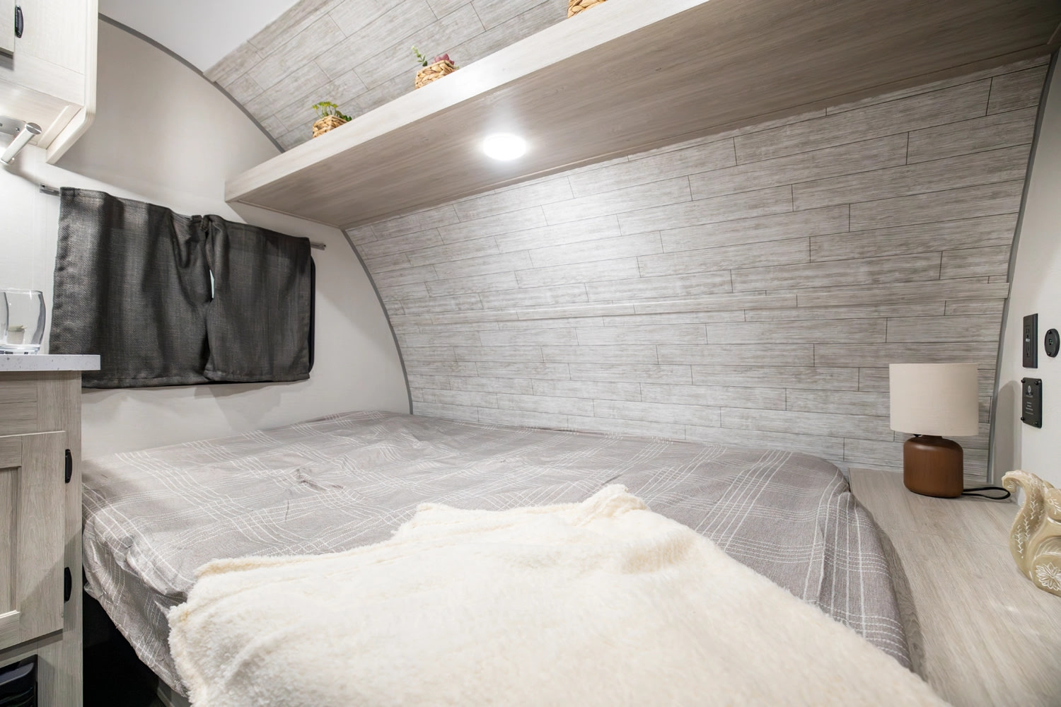 Inviting rv rental bedroom features a comfy bed, wood-paneled walls, an overhead shelf with lights, and a window.. Forest River Aurora Aurora Light 2026