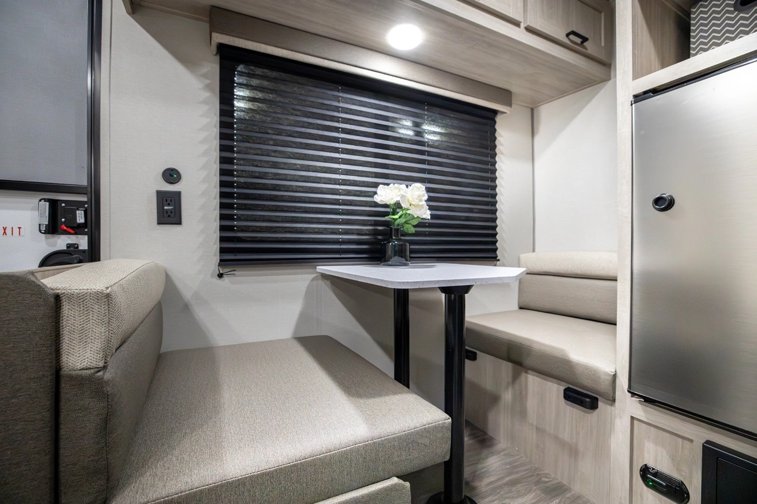 This RV rental shows a well-lit dinette with comfortable booth seating, a central table, window with blinds, and a compact fridge.. Forest River Aurora Aurora Light 2026