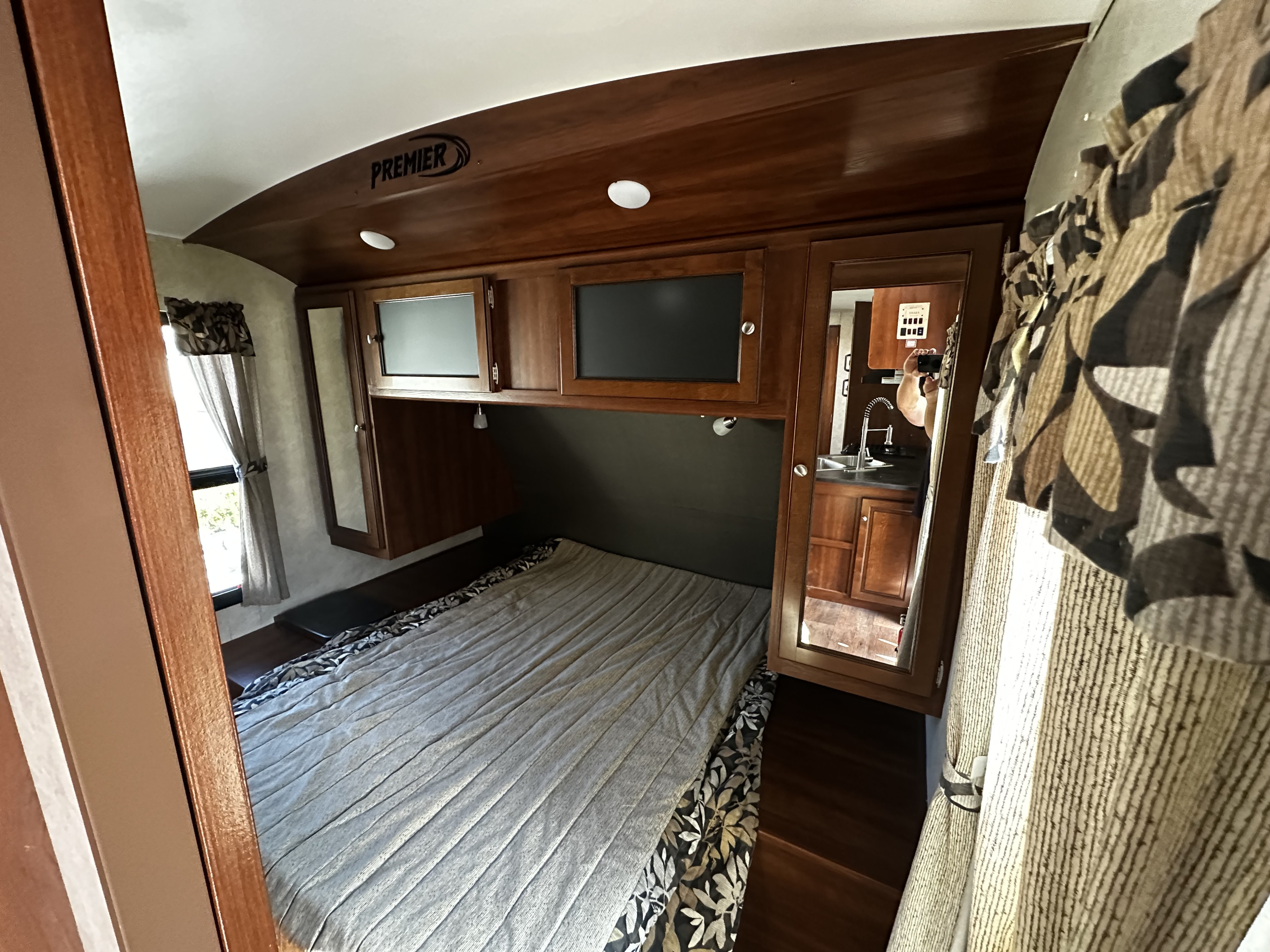 Cozy RV rental bedroom with a large bed, wooden cabinets, and a mirrored closet reflecting a kitchen area. Ideal camper stay.. Keystone RV Bullet Premier 2015