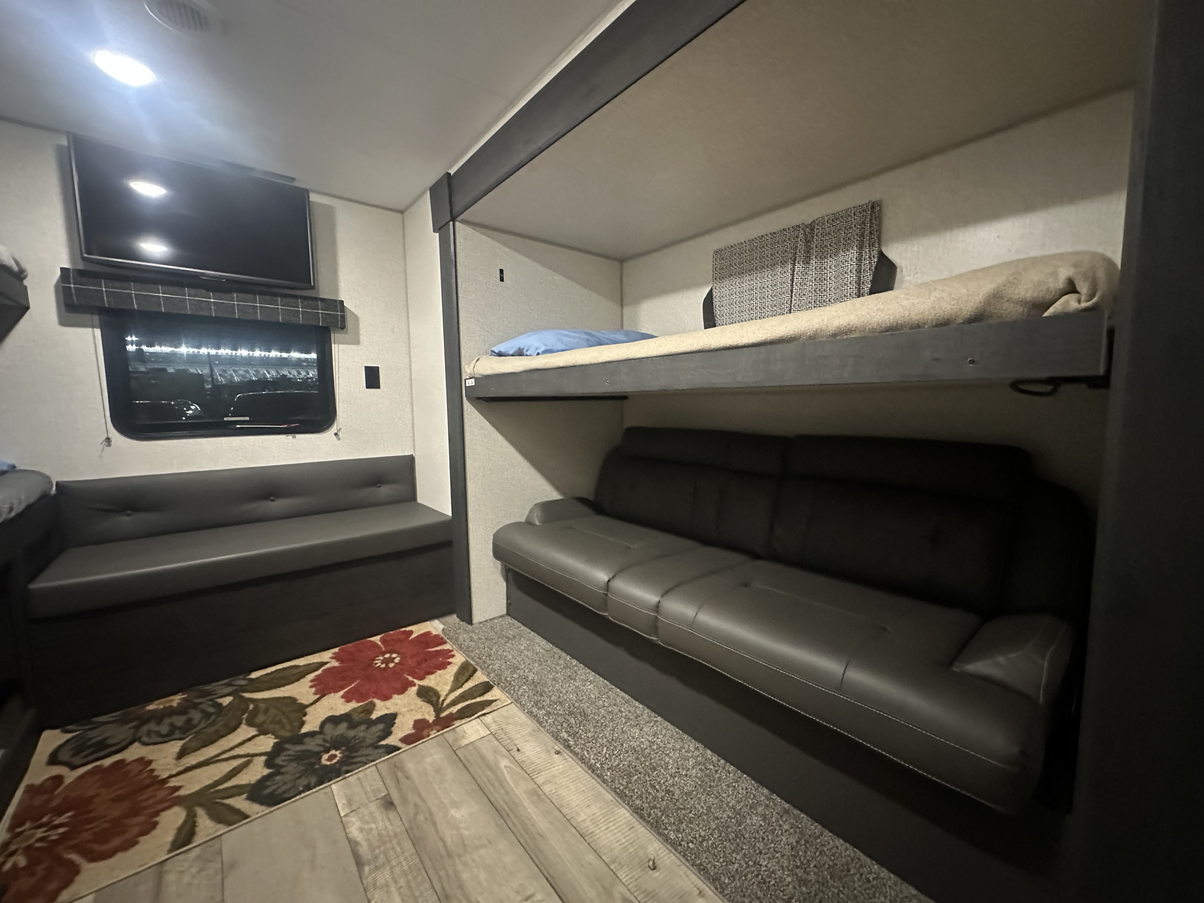 This cozy RV rental offers a functional living space with bunk beds, two gray sofas, a TV, and a floral rug.. K-Z Sportsmen SE 332BHKSE 2022