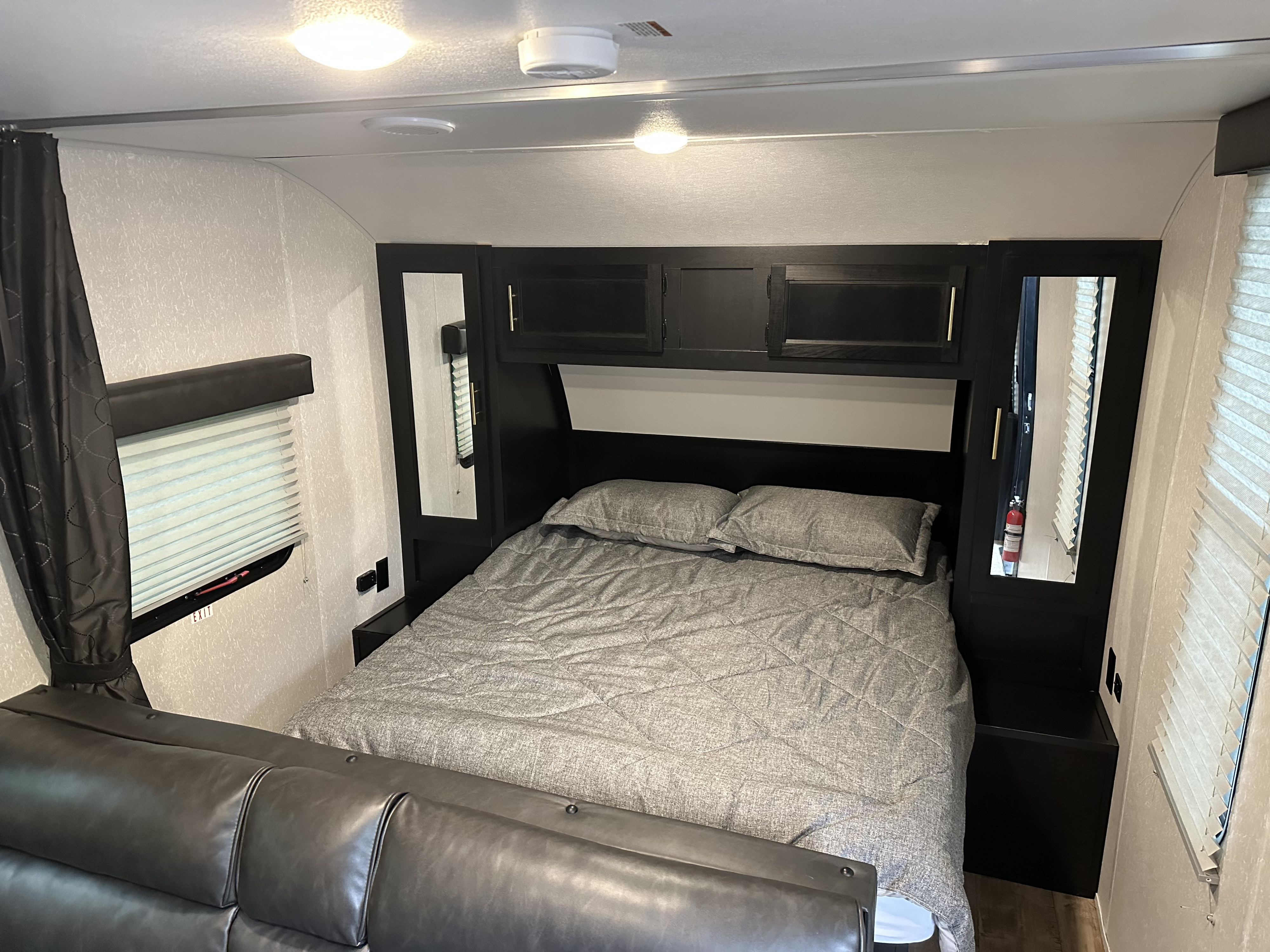 Cozy RV rental bedroom featuring a bed with gray bedding, overhead storage, side mirrors, and a comfortable sofa.. Forest River Patriot Edition 2022