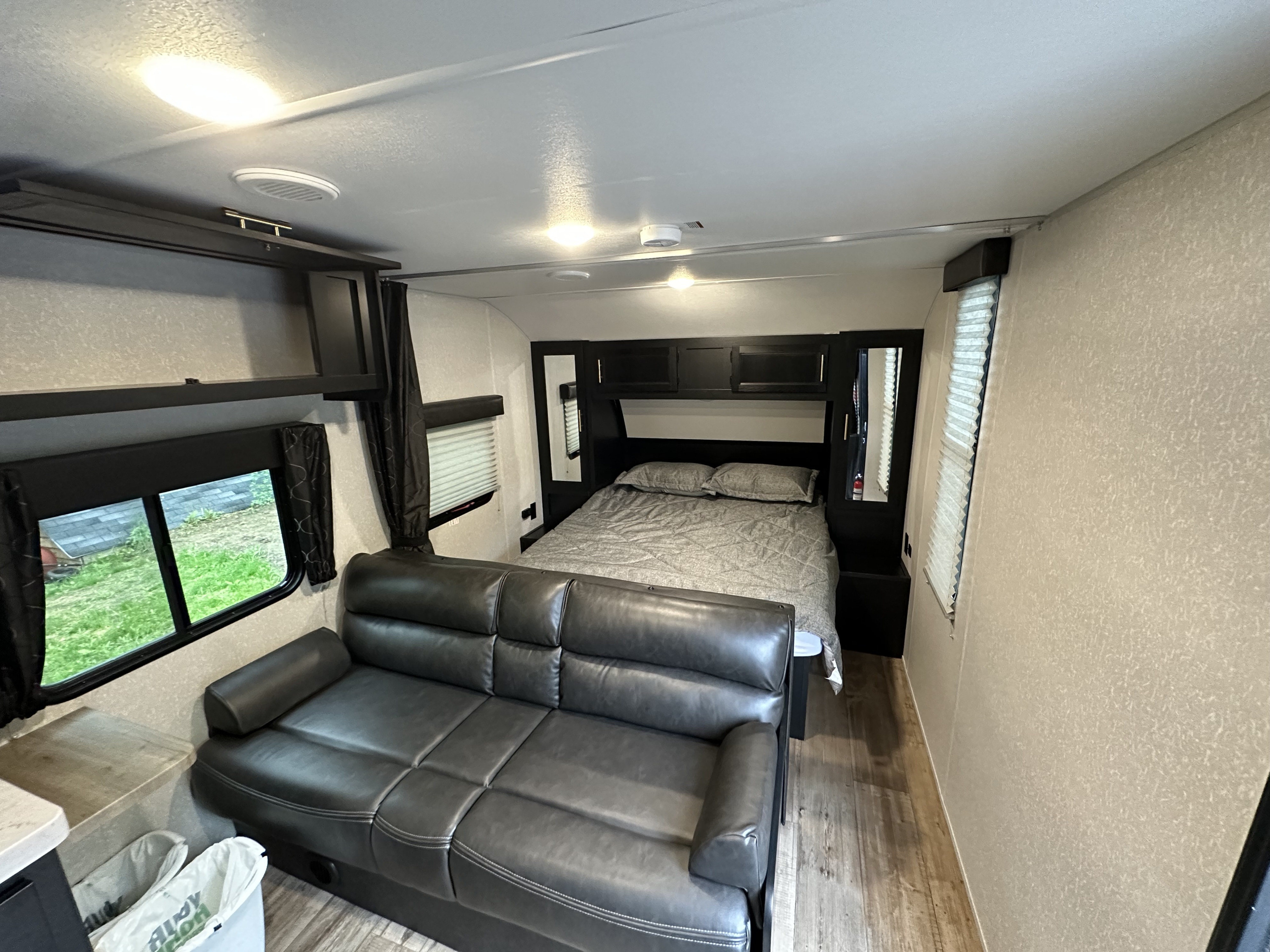 Interior of an RV rental showing a dark grey sofa in the living area leading to a comfortable bed in the bedroom.. Forest River Patriot Edition 2022