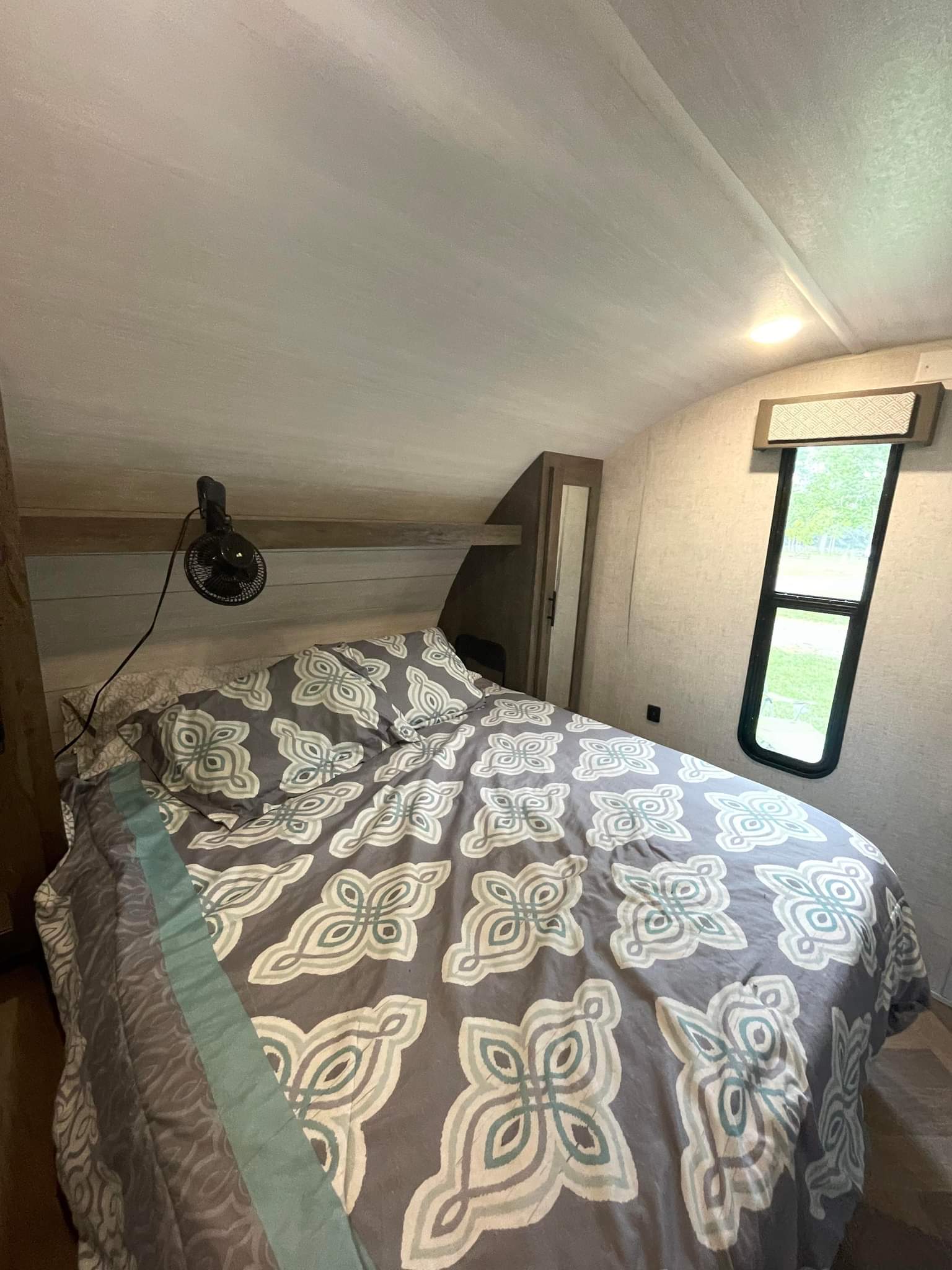 Comfortable rv rental bedroom featuring a patterned bed, bedside fan, and a window for scenic views.. Forest River Wildwood X-Lite 2021