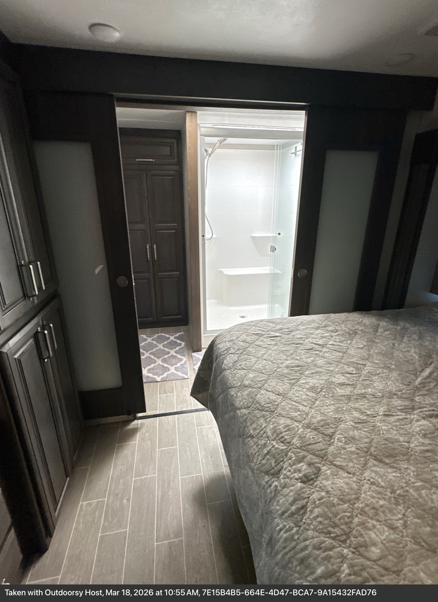 Comfortable RV rental bedroom with a cozy bed, dark cabinets, and an ensuite bathroom featuring a modern shower. Perfect for your travel adventures.. Keystone RV Alpine 2021