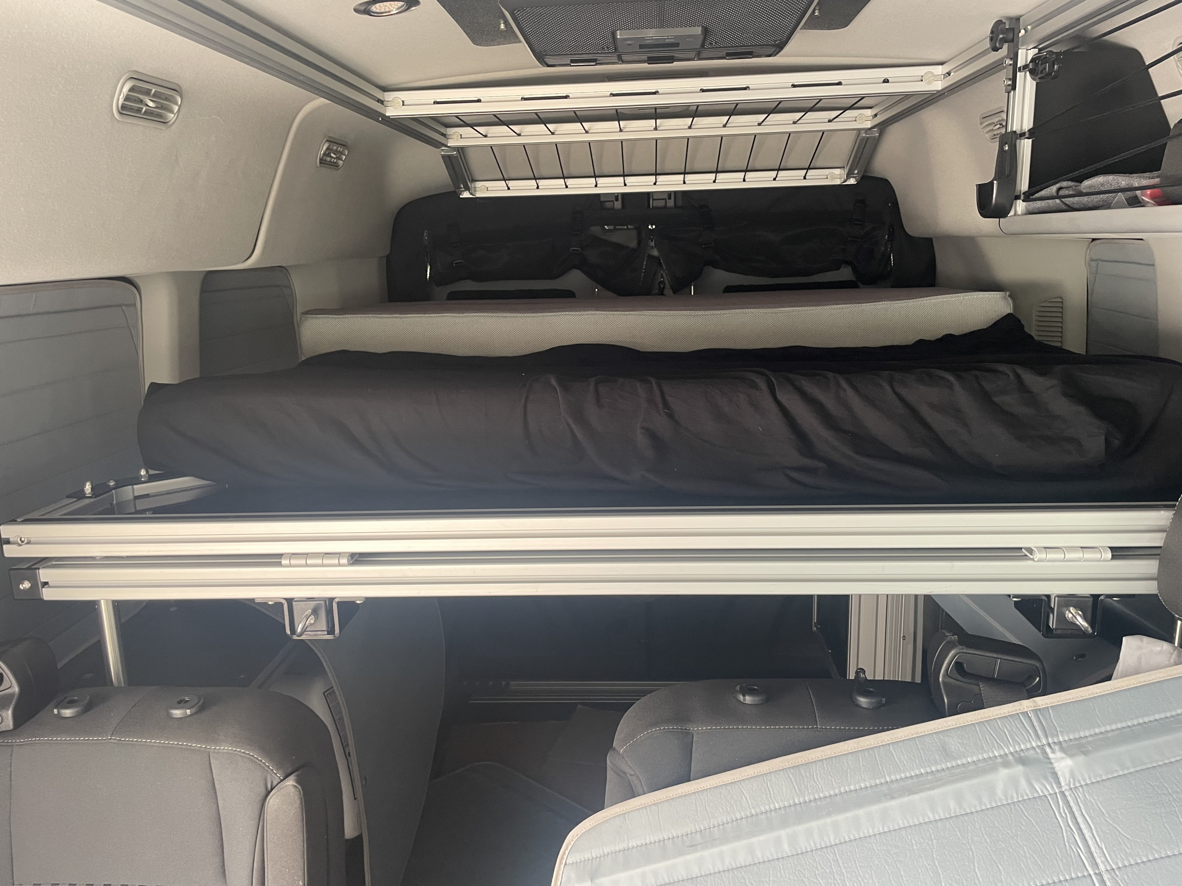 Interior of an RV rental featuring a two-tier bunk bed system, upper storage rack, and rear seating, ideal for compact travel.. Ford Transit Custom 2023