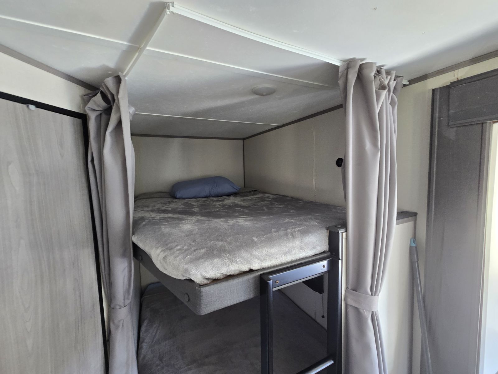 Cozy RV rental bunk beds with privacy curtains, featuring soft grey bedding and a blue pillow, ideal for compact sleeping areas.. Coleman Lantern LT 26BH 2022
