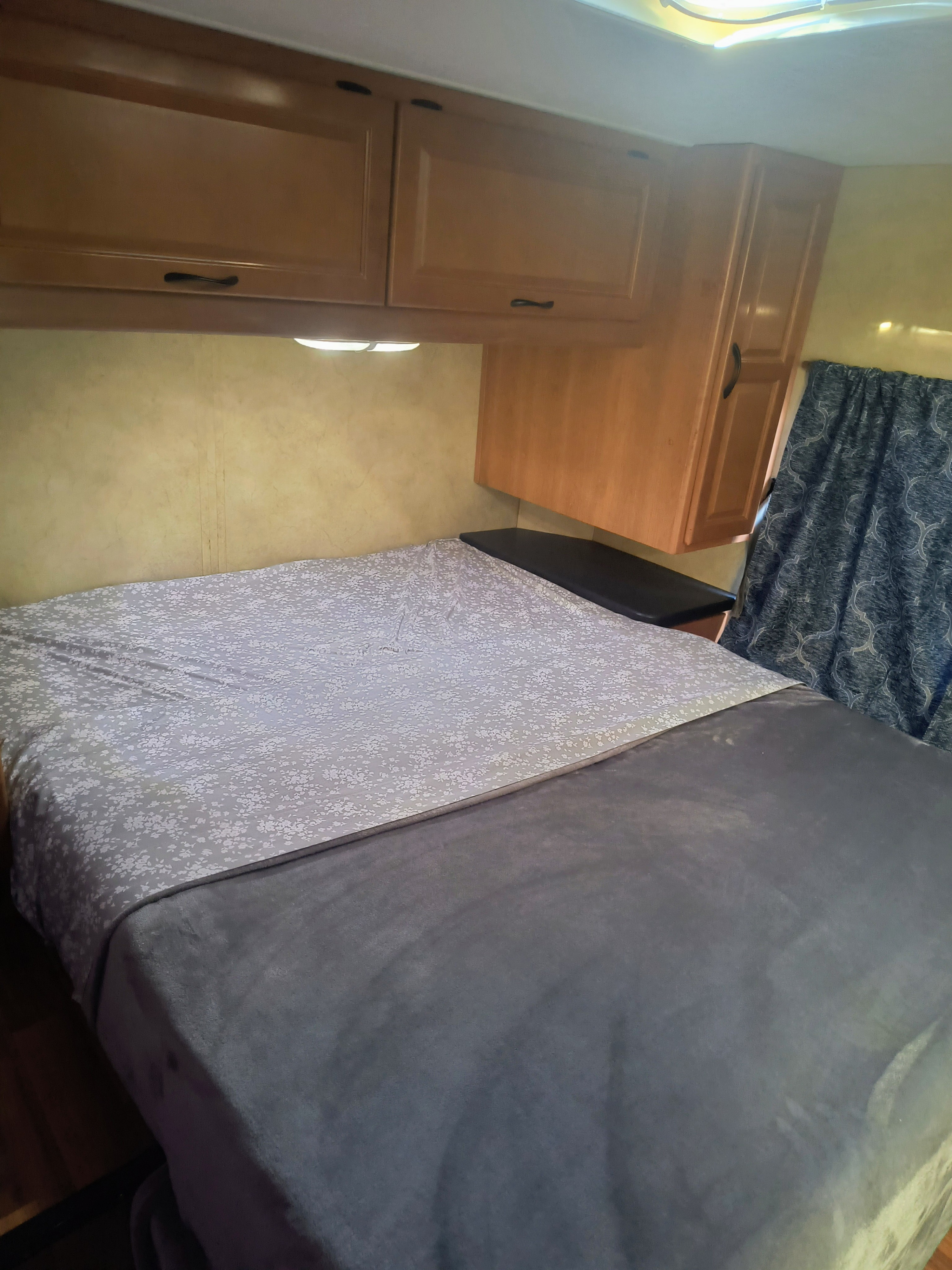 RV rental bedroom: Features a comfortable bed with patterned sheets, overhead cabinets, and a curtain for privacy.. thor majestic 2014