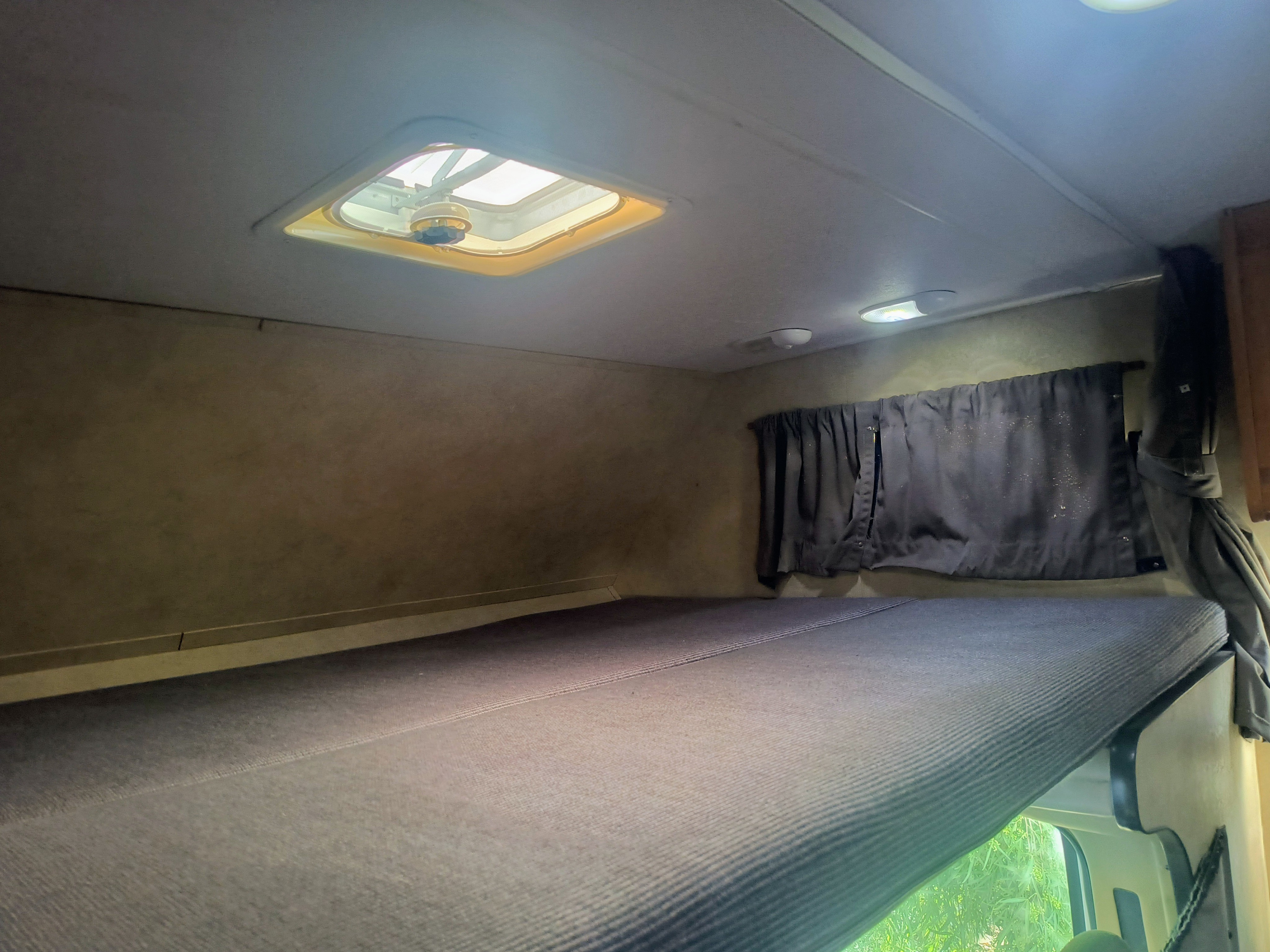 Inside an rv rental: a comfortable bunk bed with a roof vent, overhead lighting, and privacy curtain.. thor majestic 2014