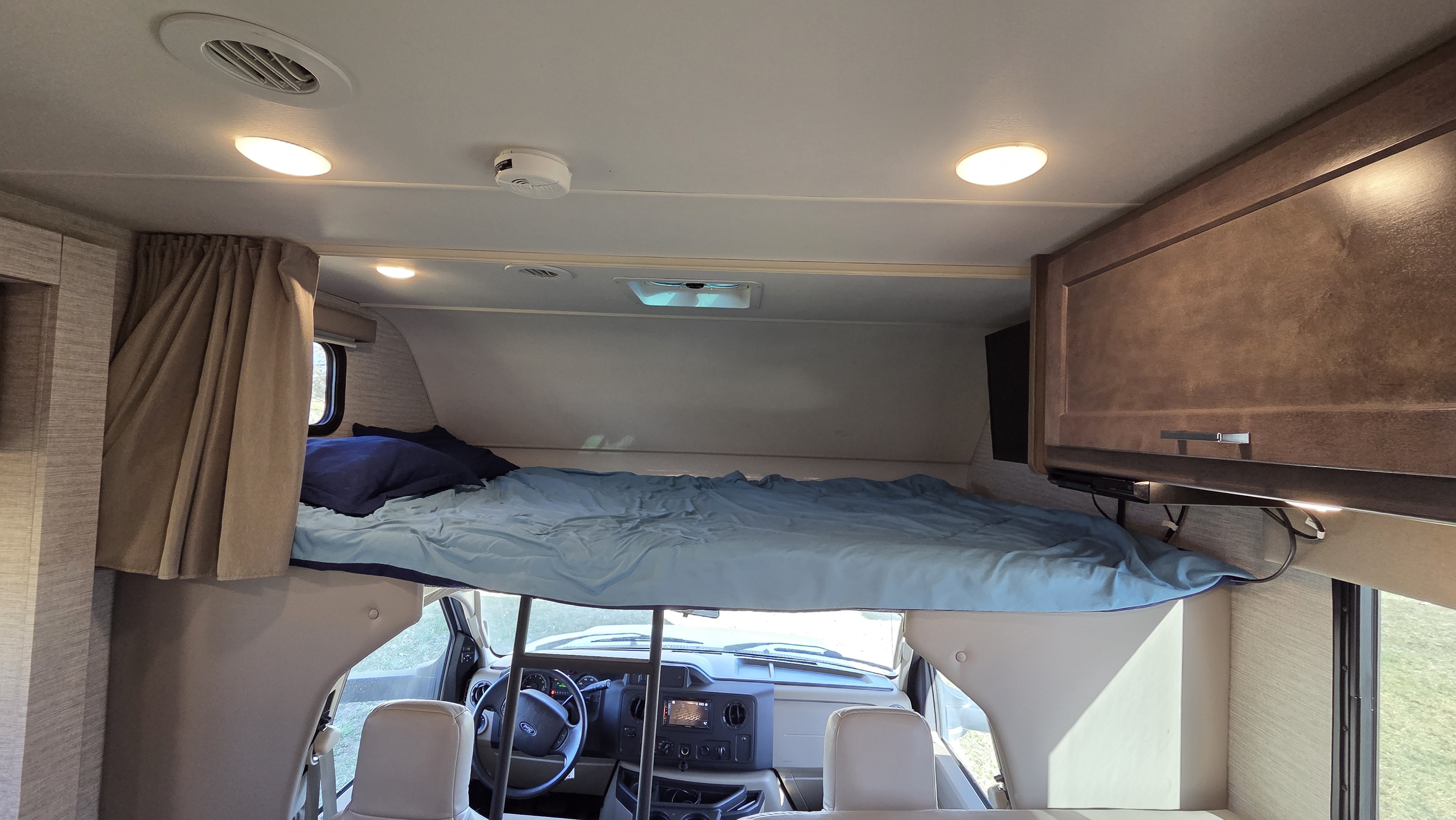 RV rental interior: Cozy cab-over bunk bed with blue bedding, situated above the RV's driver's cabin.. Winnebago Minnie Winnie 2021