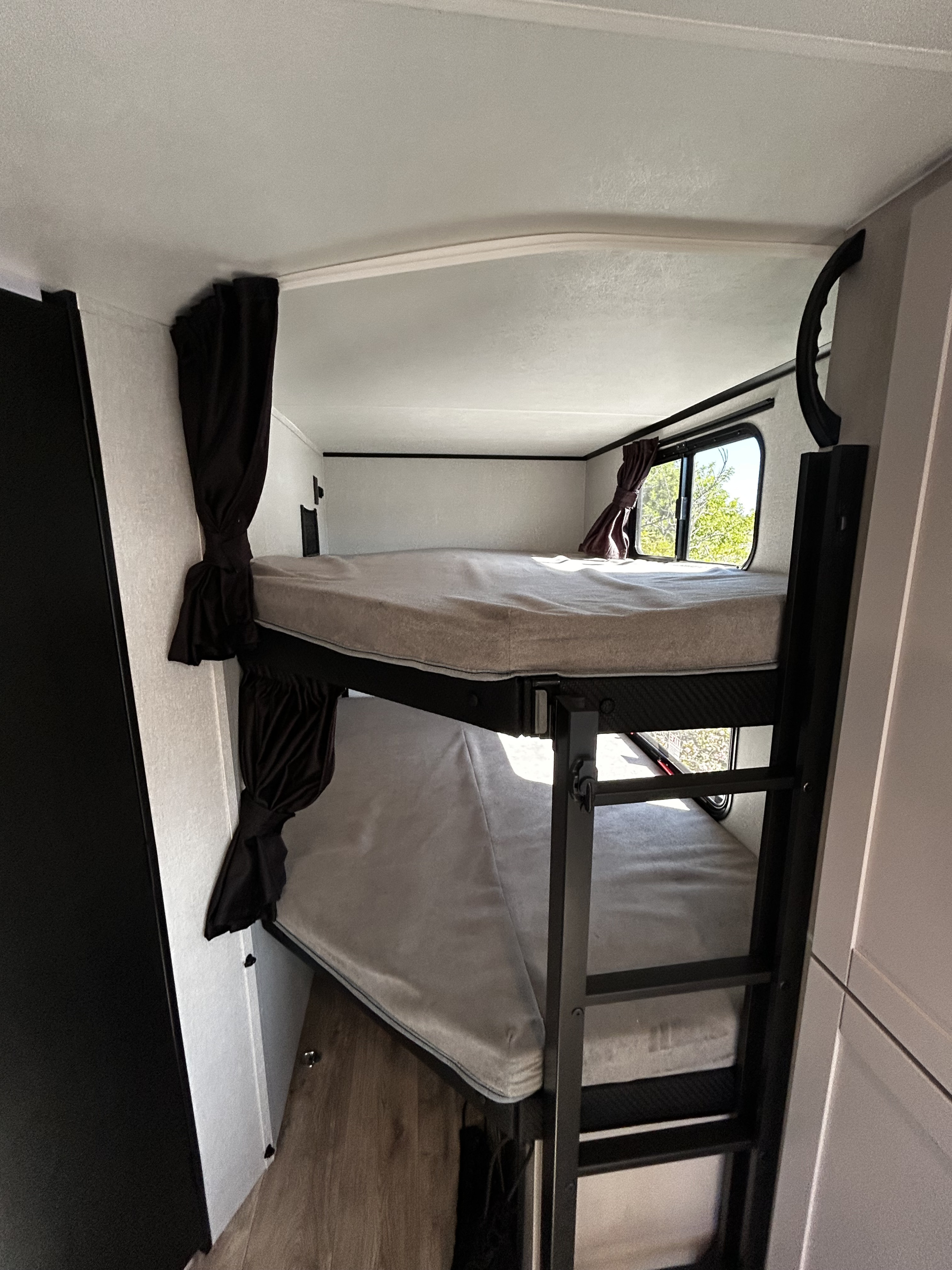 Cozy bunk beds in an RV rental, featuring black metal frame, soft mattresses, tied-back curtains, and a window view.. Jayco 29BHB 2026
