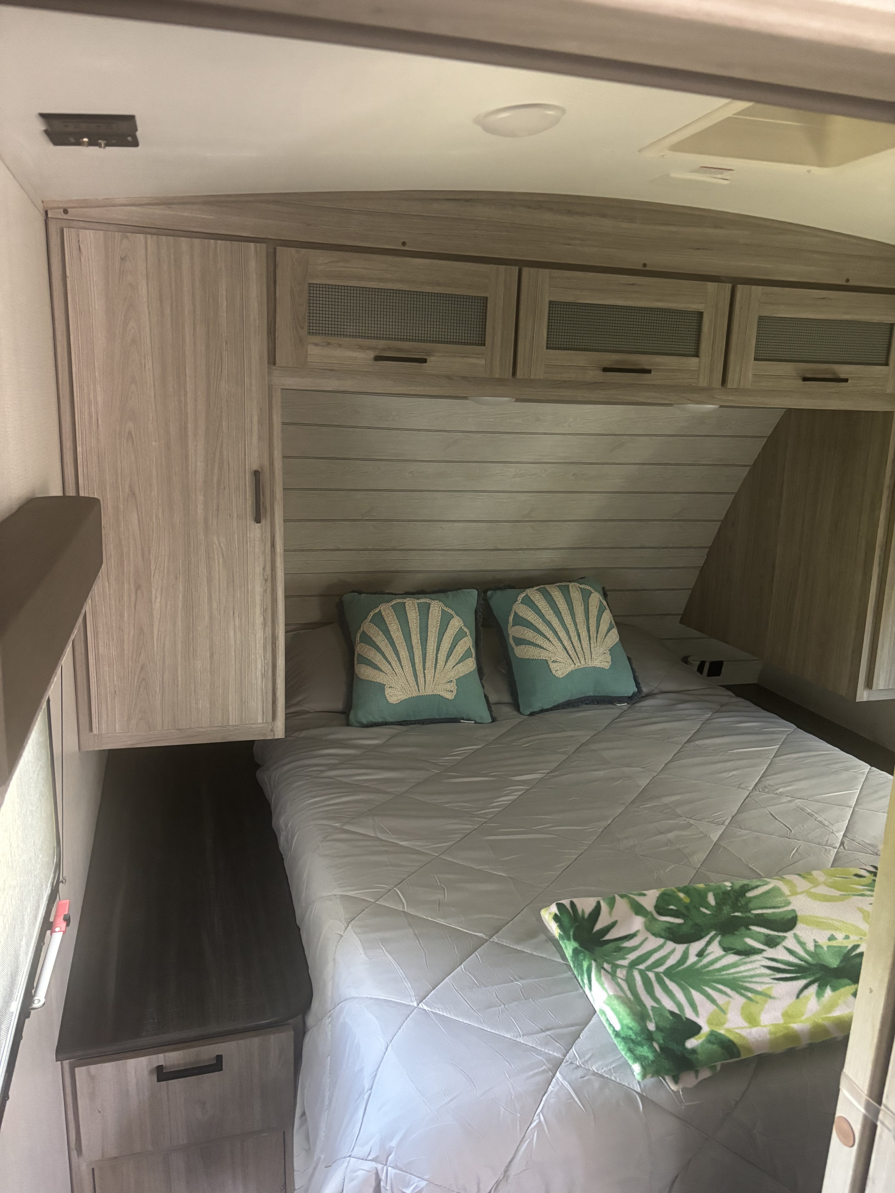 Cozy RV rental bedroom features a comfy bed with seashell pillows, overhead cabinets, and a tropical blanket.. Keystone RV Passport GT 2022