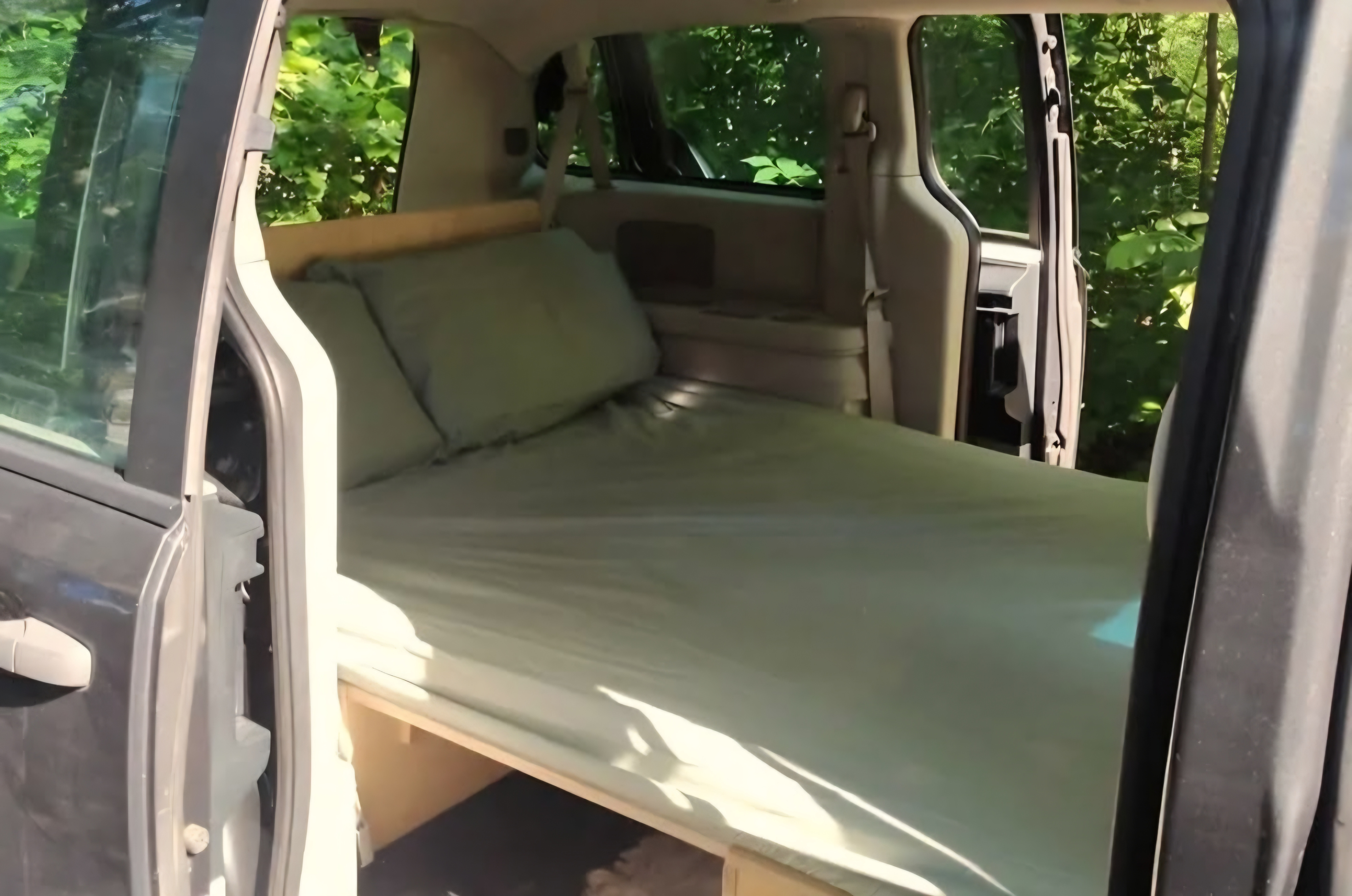 Cozy RV rental van conversion: a simple bed setup with green sheets & pillows, perfect for camping or road trips.. Dodge Grand Caravan 2012