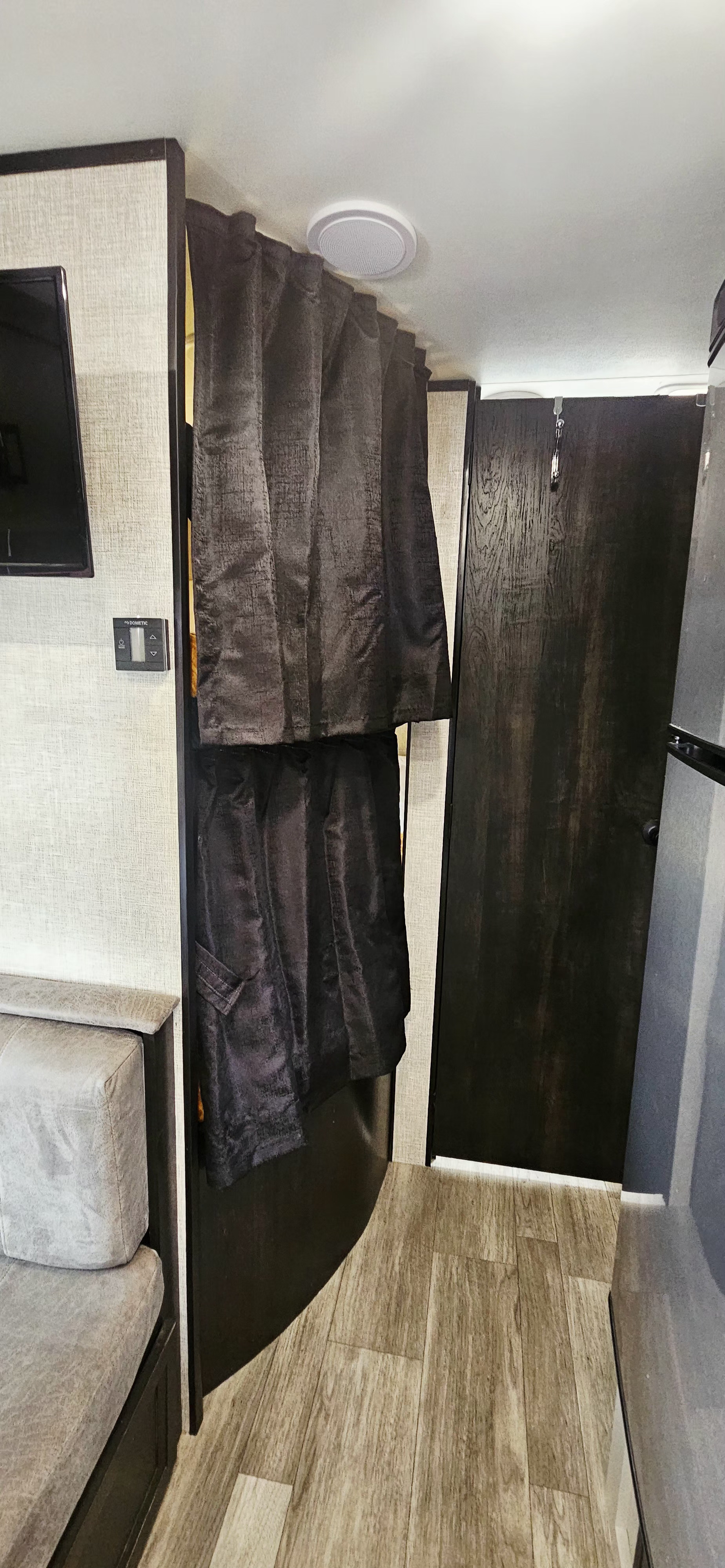 RV rental interior featuring a gray sofa, TV, Dometic panel, and dark privacy curtains next to a dark wood door.. Jayco Jay Flight SLX 2022