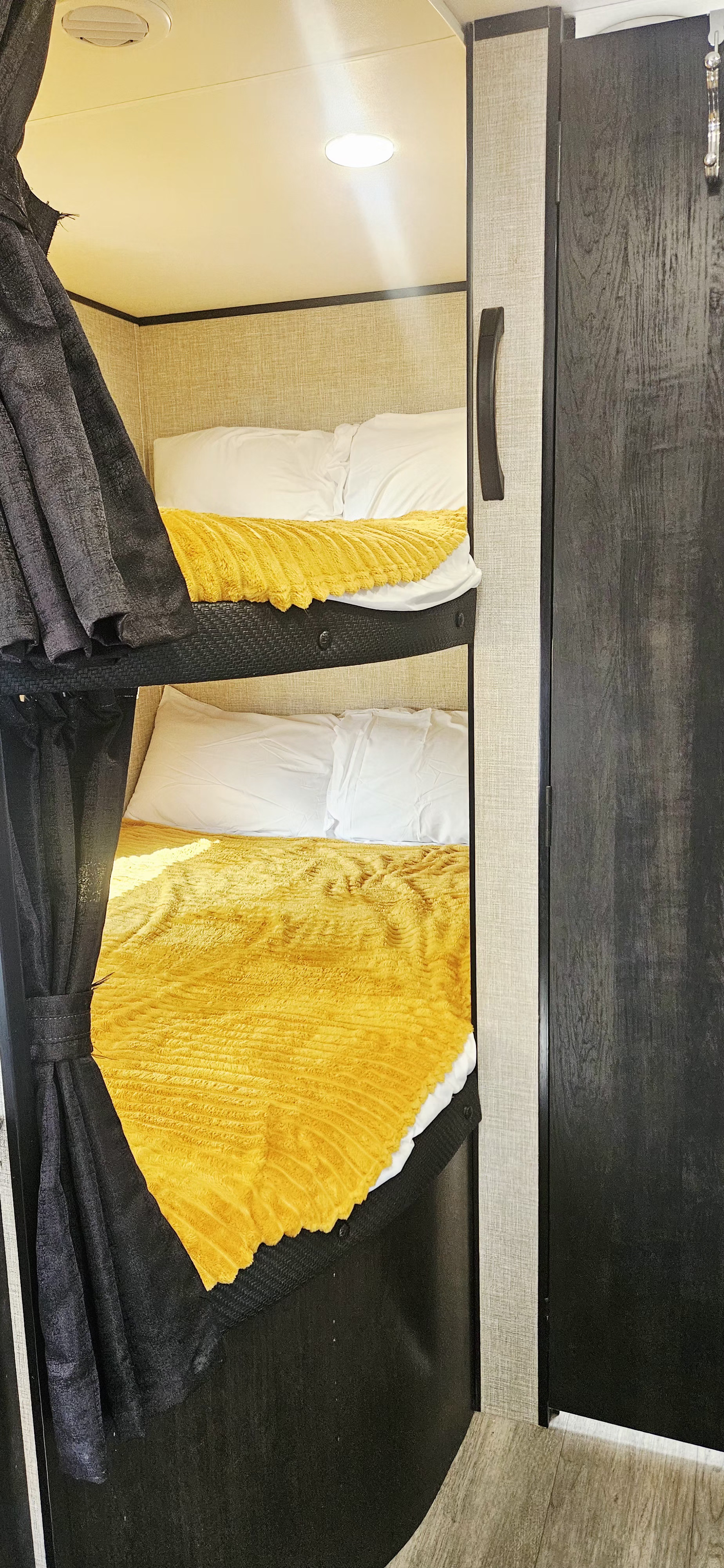 Cozy bunk beds with bright yellow blankets & black privacy curtains in an RV rental. A well-lit, compact sleeping area for travelers.. Jayco Jay Flight SLX 2022