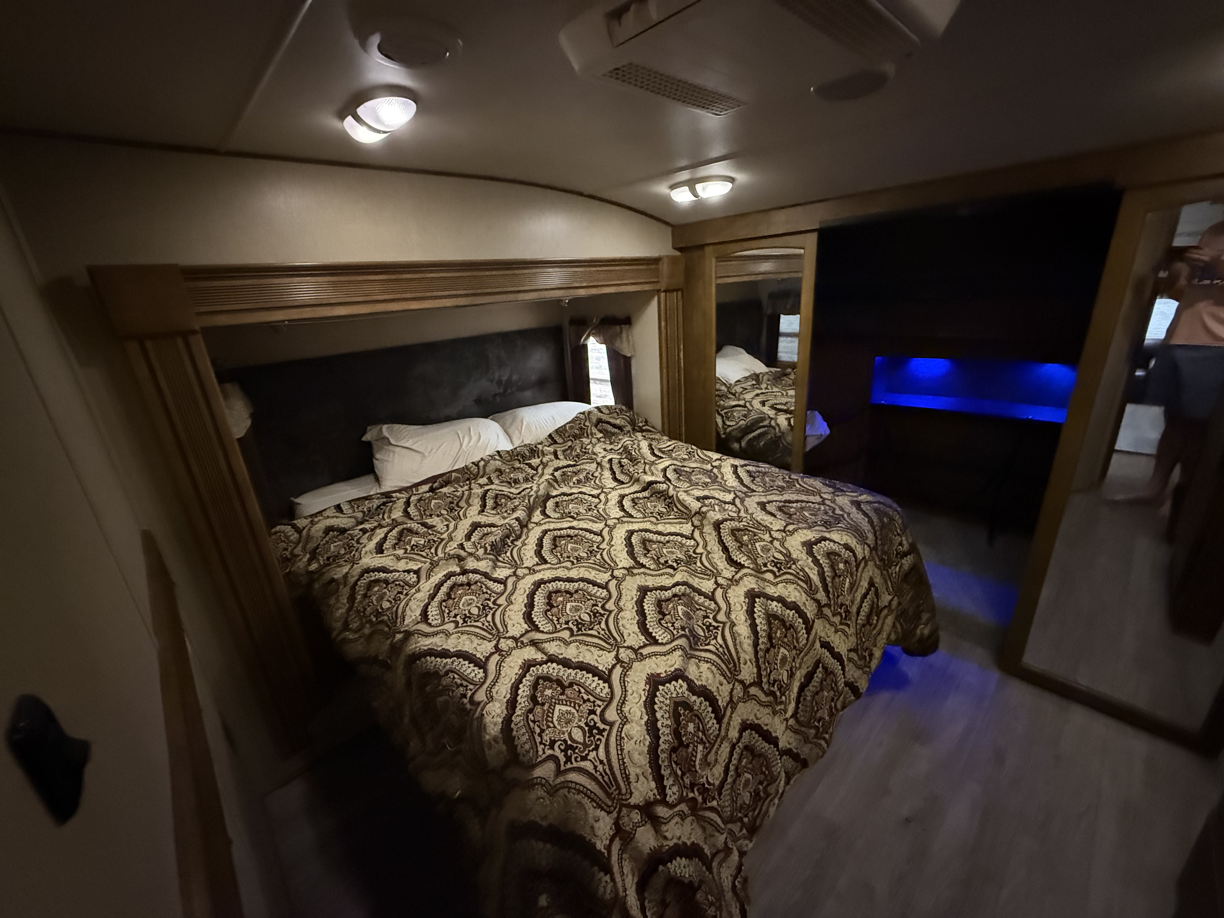 Cozy RV rental bedroom with a large bed, patterned comforter, and mirrors, illuminated by ambient blue light.. Grand Design Reflection 2015
