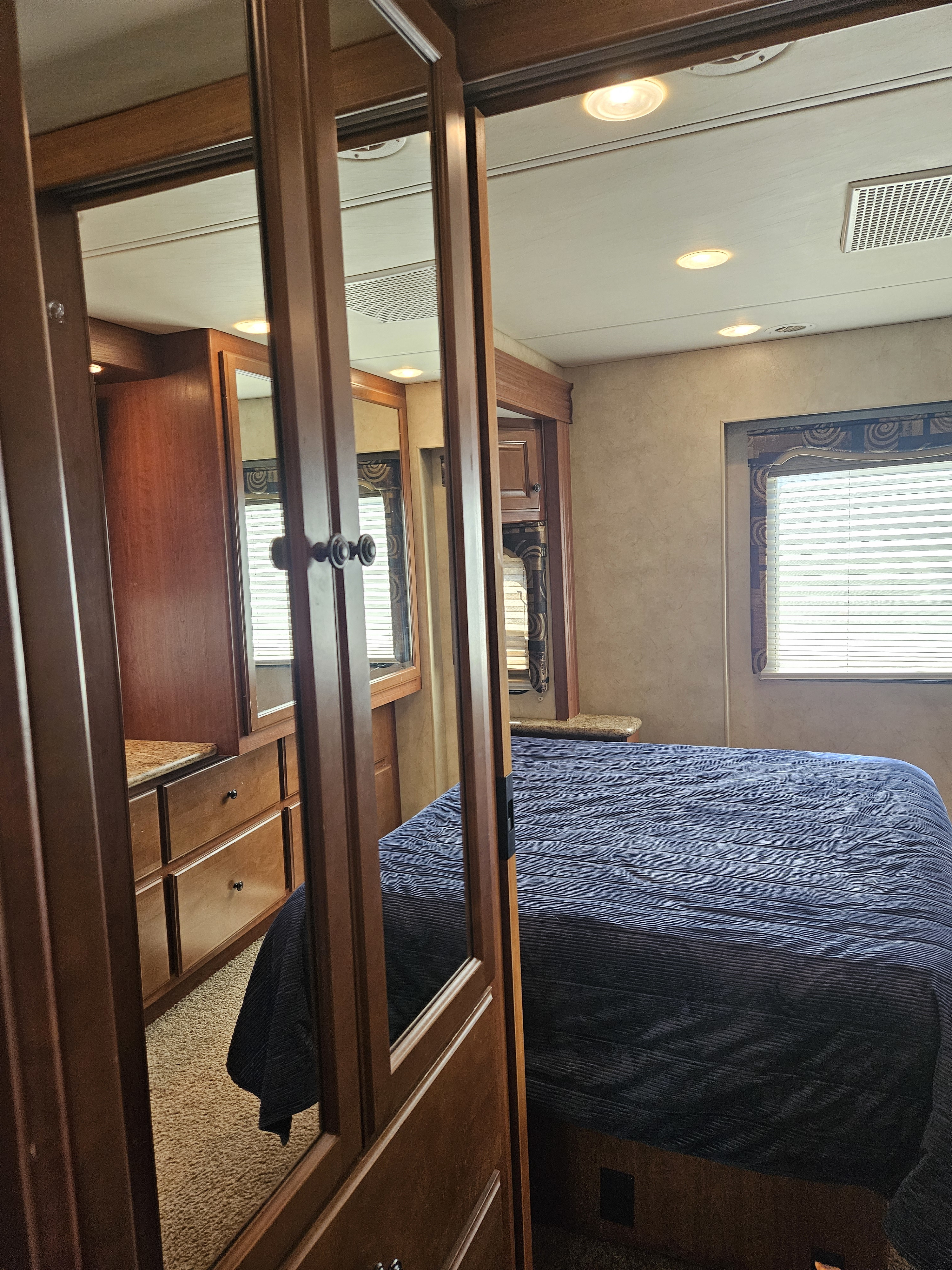 Cozy RV rental bedroom with a comfortable bed, mirrored closet doors, and wooden cabinets for storage.. Four Winds Windsport 2011