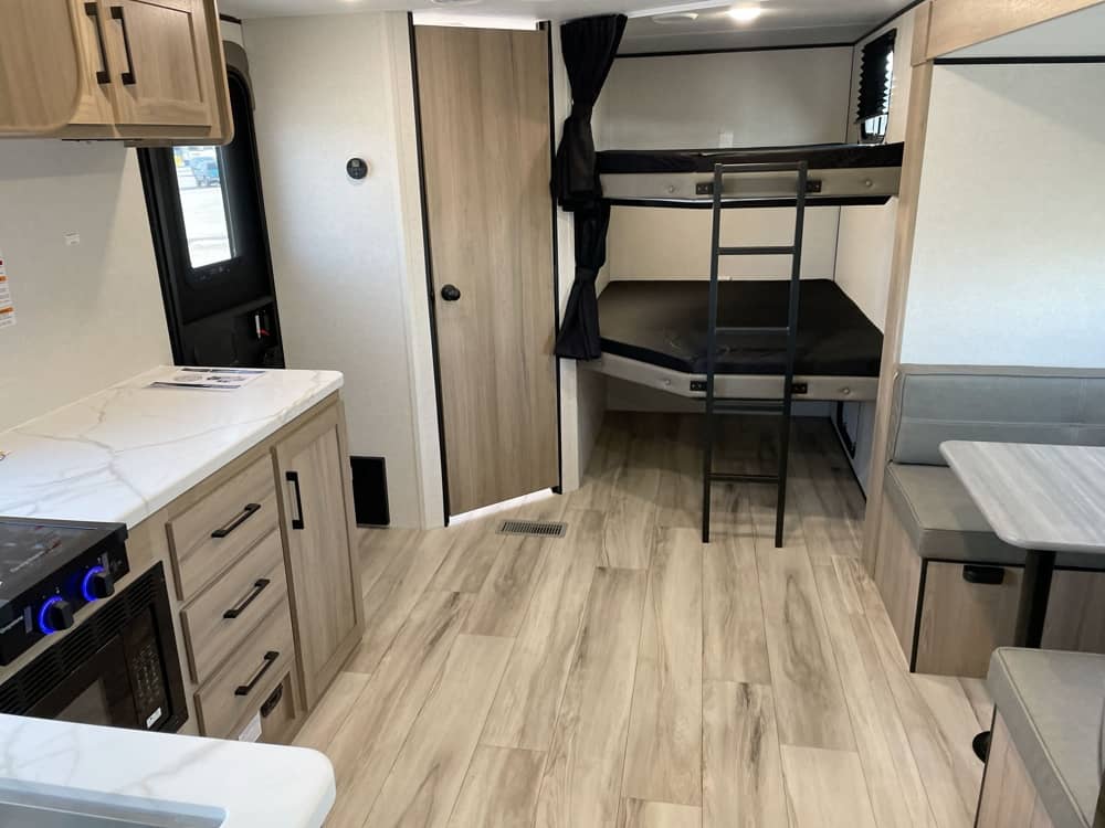 Clean rv rental interior featuring a kitchen with counter & appliances, bunk beds with ladder, and dinette area.. Keystone RV Coleman Light 2025