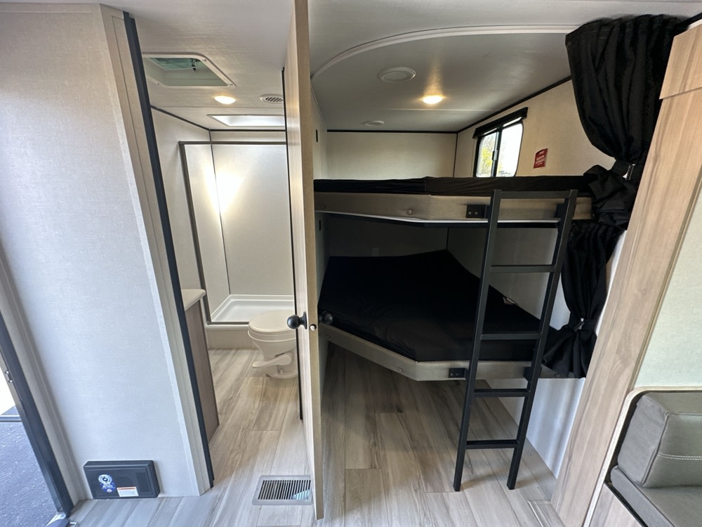 Inside an RV rental: a compact bathroom with shower & toilet, plus bunk beds with a ladder & privacy curtains. Ideal for family trips.. Keystone RV Coleman Light 2025
