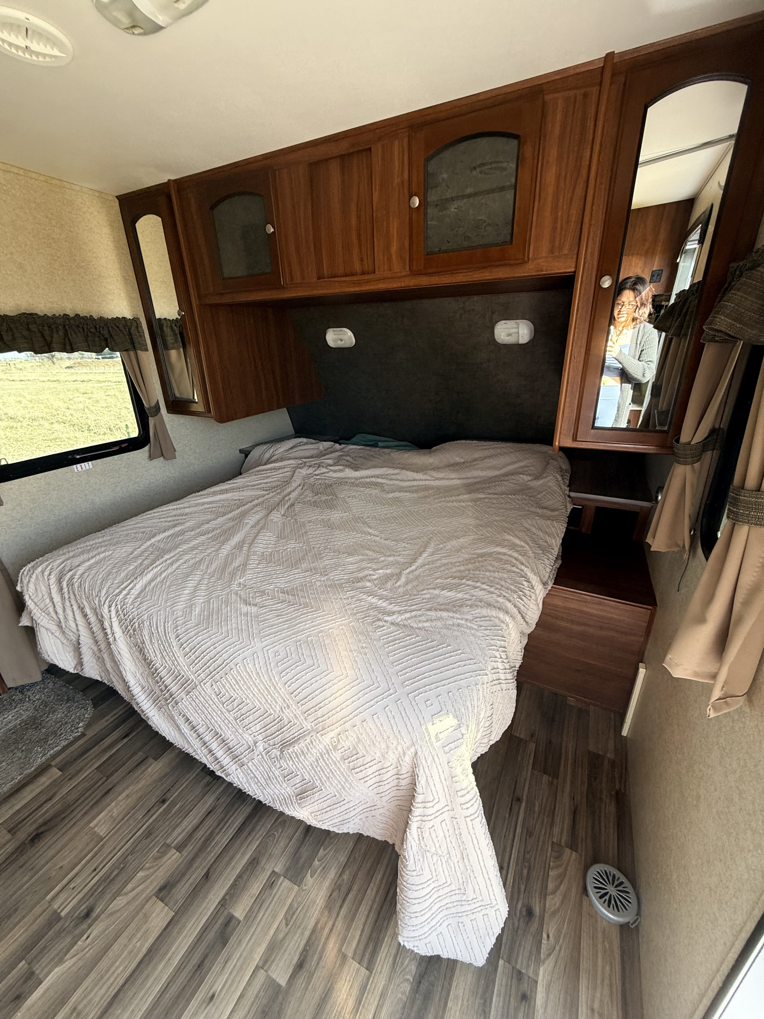 RV rental bedroom featuring a comfortable bed, wooden cabinets, window with outdoor view, and a mirror on the wall.. Heartland RVs North Trail 2014