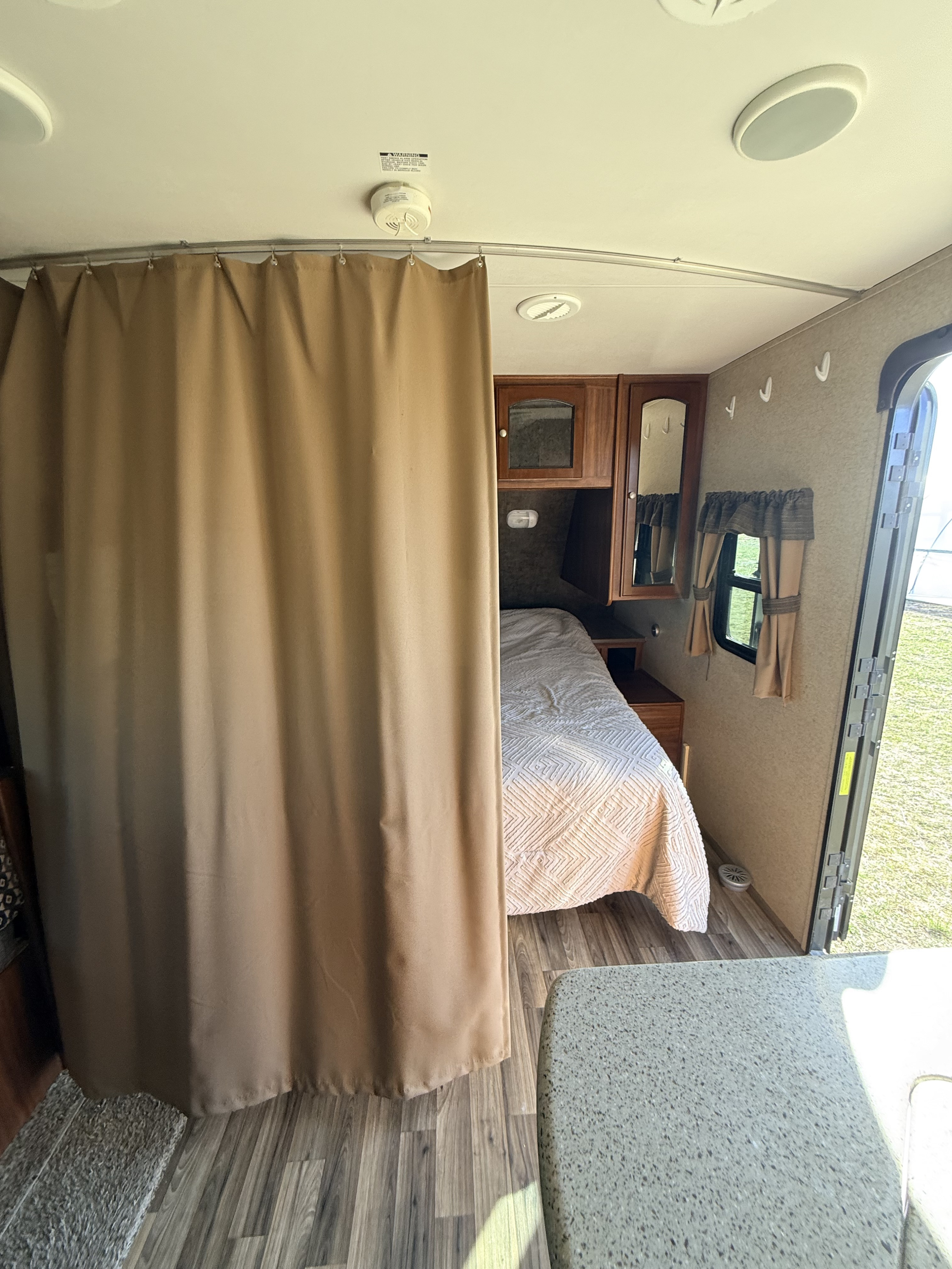 Inside an rv rental: a compact bedroom with a bed and cabinets, separated by a tan curtain. Features laminate flooring and an open door.. Heartland RVs North Trail 2014