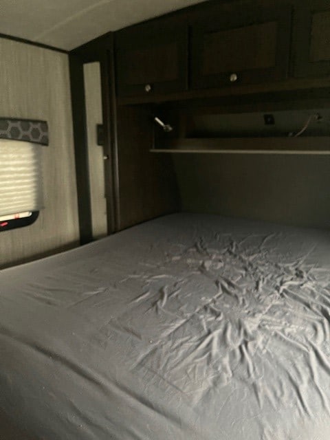 Cozy RV rental bedroom showcasing dark cabinets, a reading light, and a bed with rumpled grey sheets.. Cruiser RV Shadow Cruiser 2020