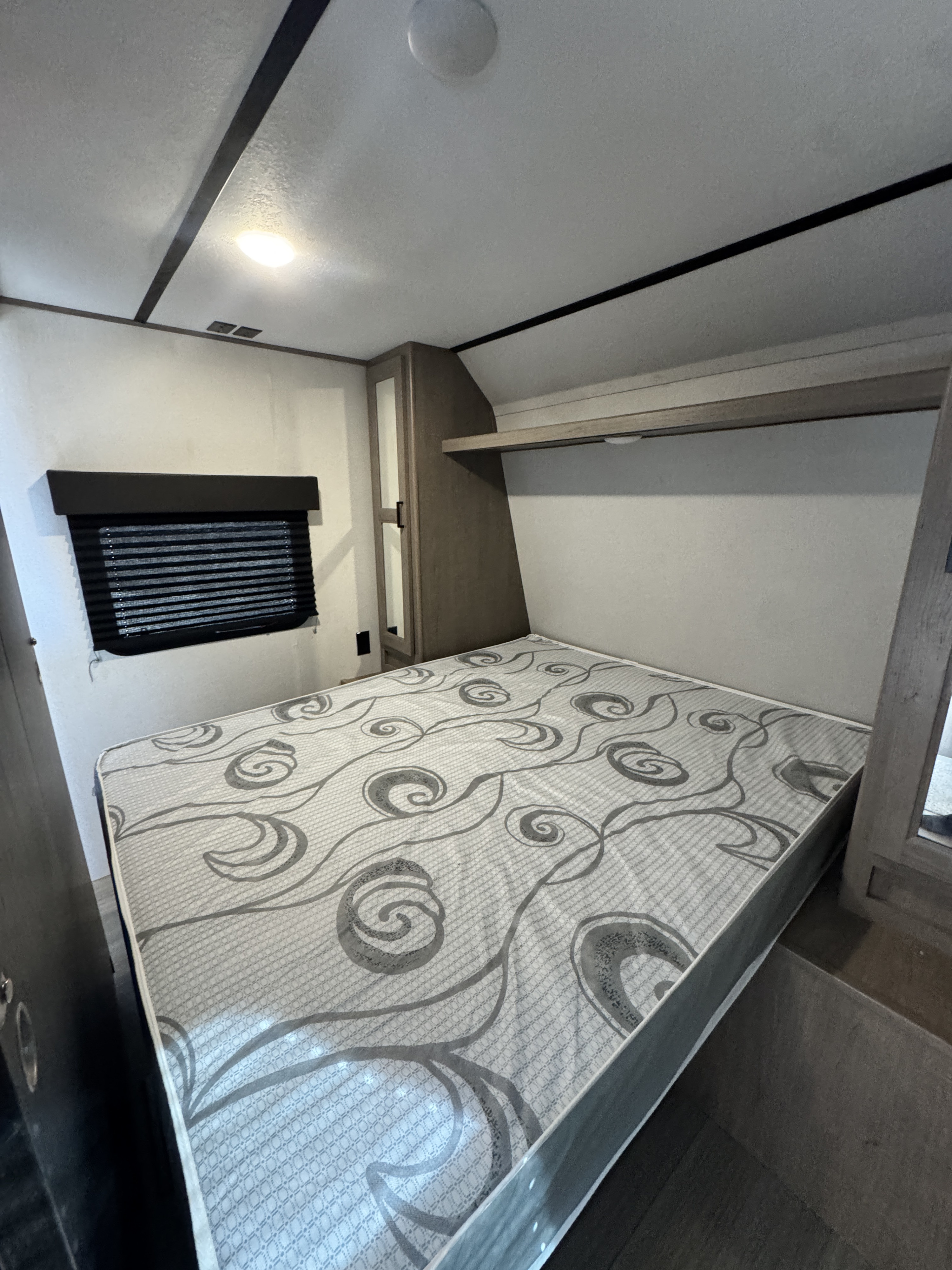 Cozy RV rental bedroom featuring a patterned mattress, window with blinds, and built-in storage, designed for compact travel.. Keystone RV Hideout 2020