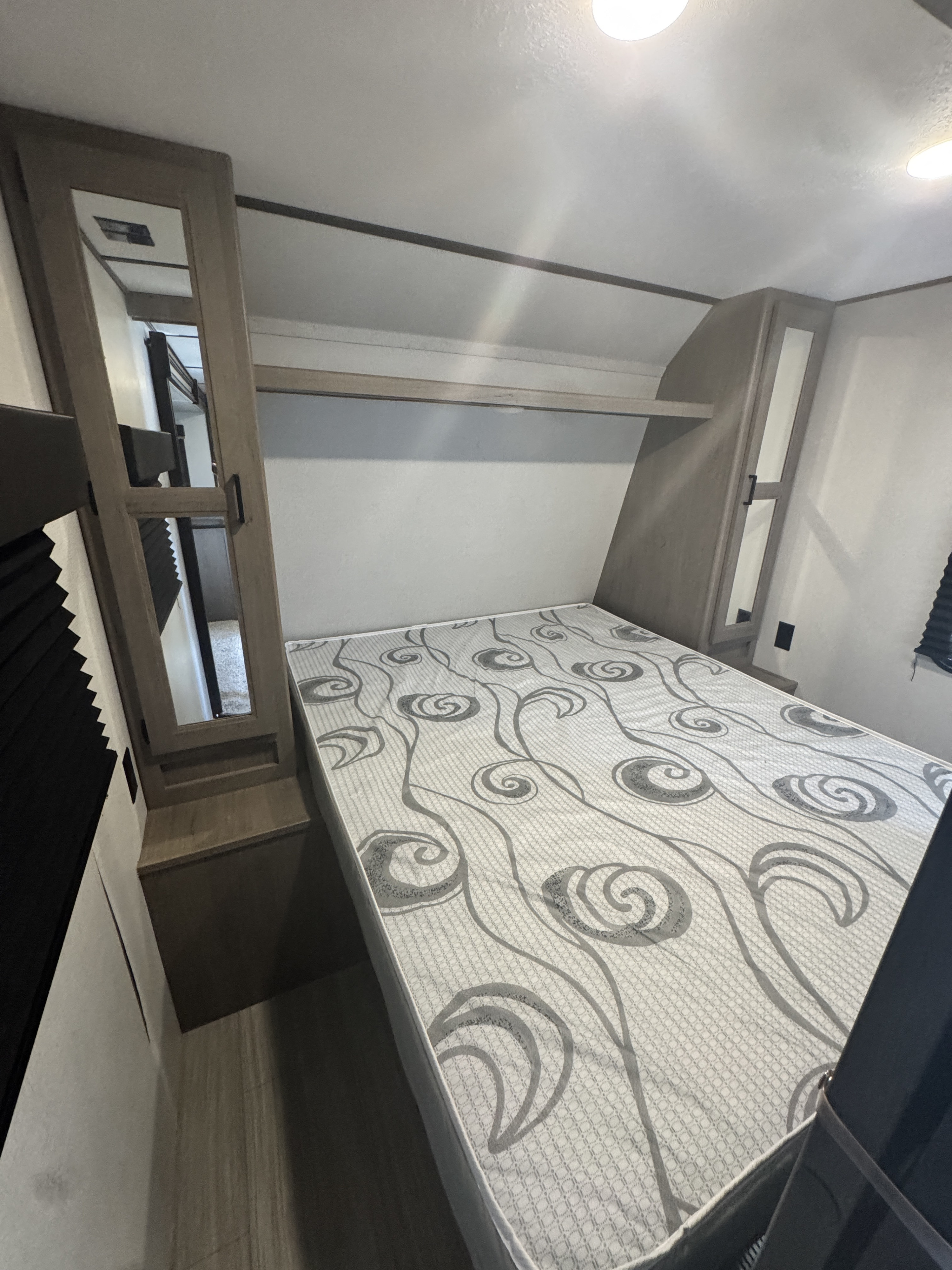 RV rental bedroom with a white mattress featuring gray swirls, flanked by mirrored cabinets and overhead storage.. Keystone RV Hideout 2020