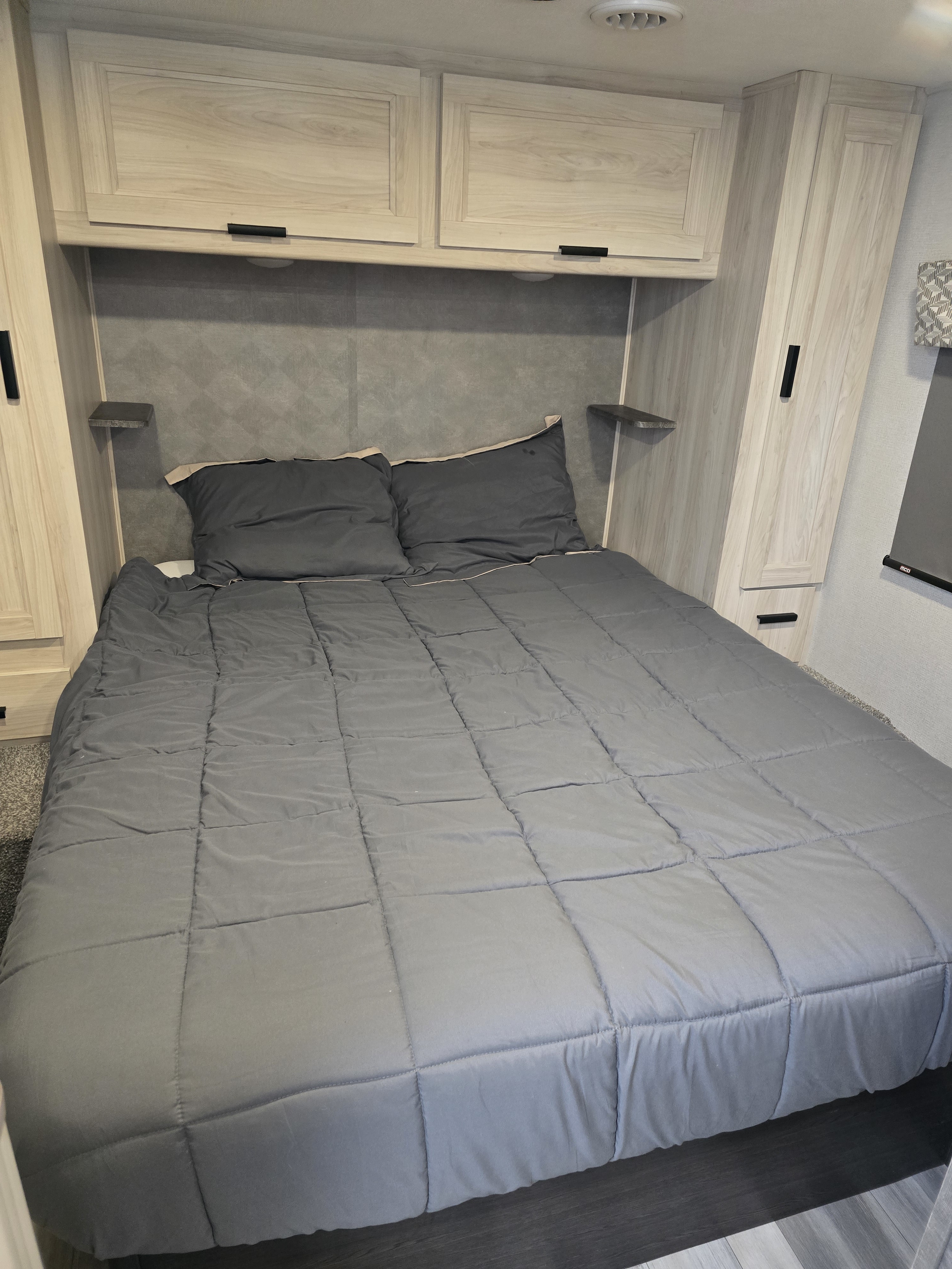 Comfortable RV rental bedroom with a grey bed, practical storage cabinets, and side shelves for a cozy stay.. Forester LE 2023