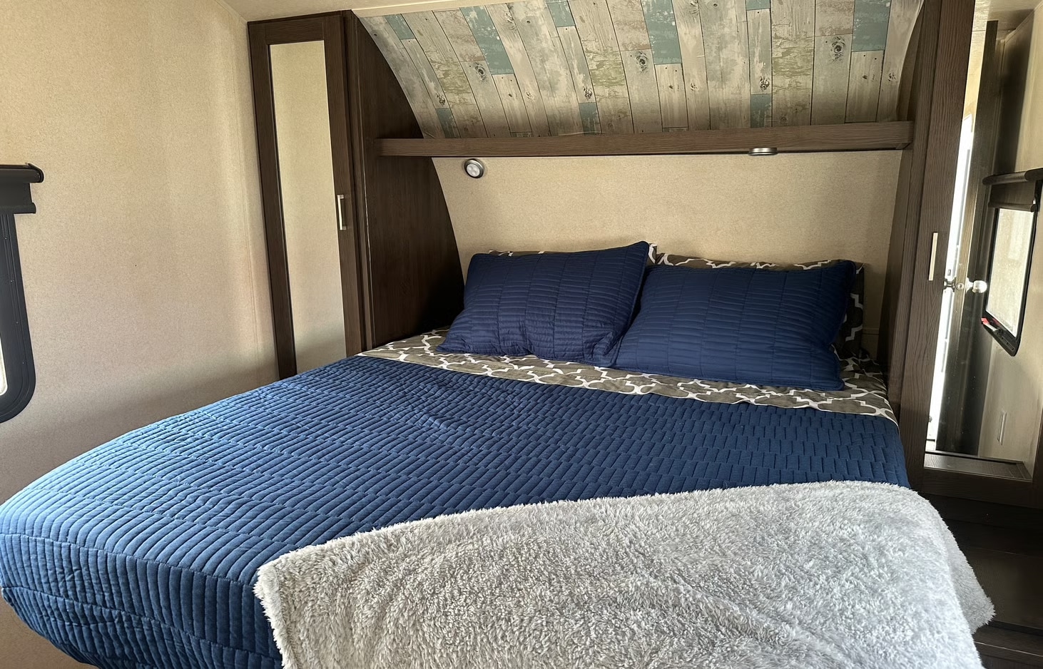 Cozy RV rental bedroom features a comfy bed with blue bedding, soft blanket, and stylish wood-look ceiling, ideal for travel.. Forest River Salem 2018