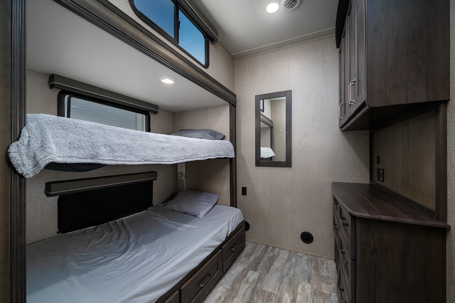 RV rental bunk room showing two bunk beds with gray bedding, dark wood cabinets/dresser, mirror, and light-toned wood-look flooring.. Grand Design Reflection 2022