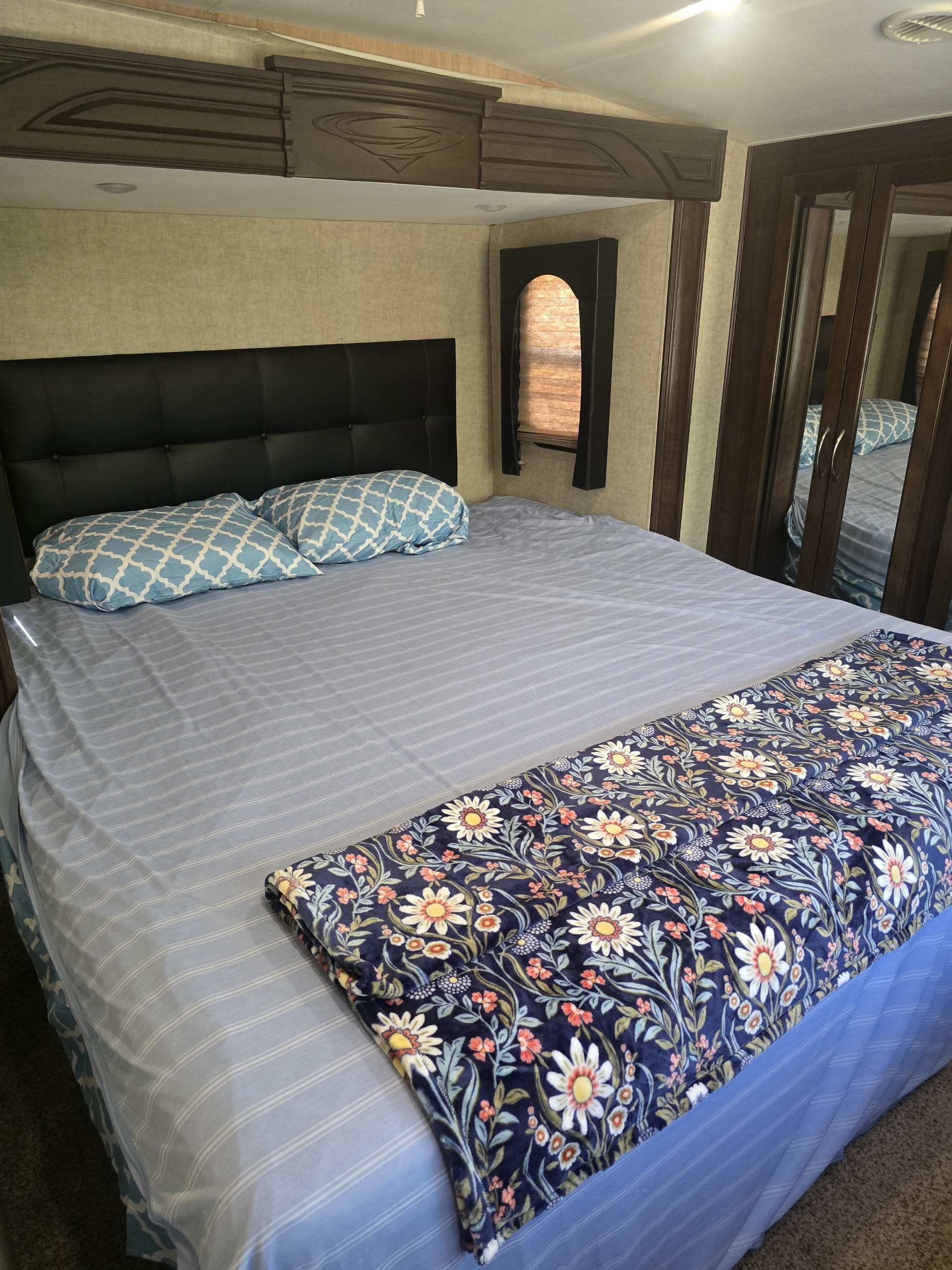 Cozy RV rental bedroom featuring a large bed, blue patterned pillows, striped sheets, and a floral blanket.. Heartland RVs Cyclone HD Edition Toy Hauler 2015