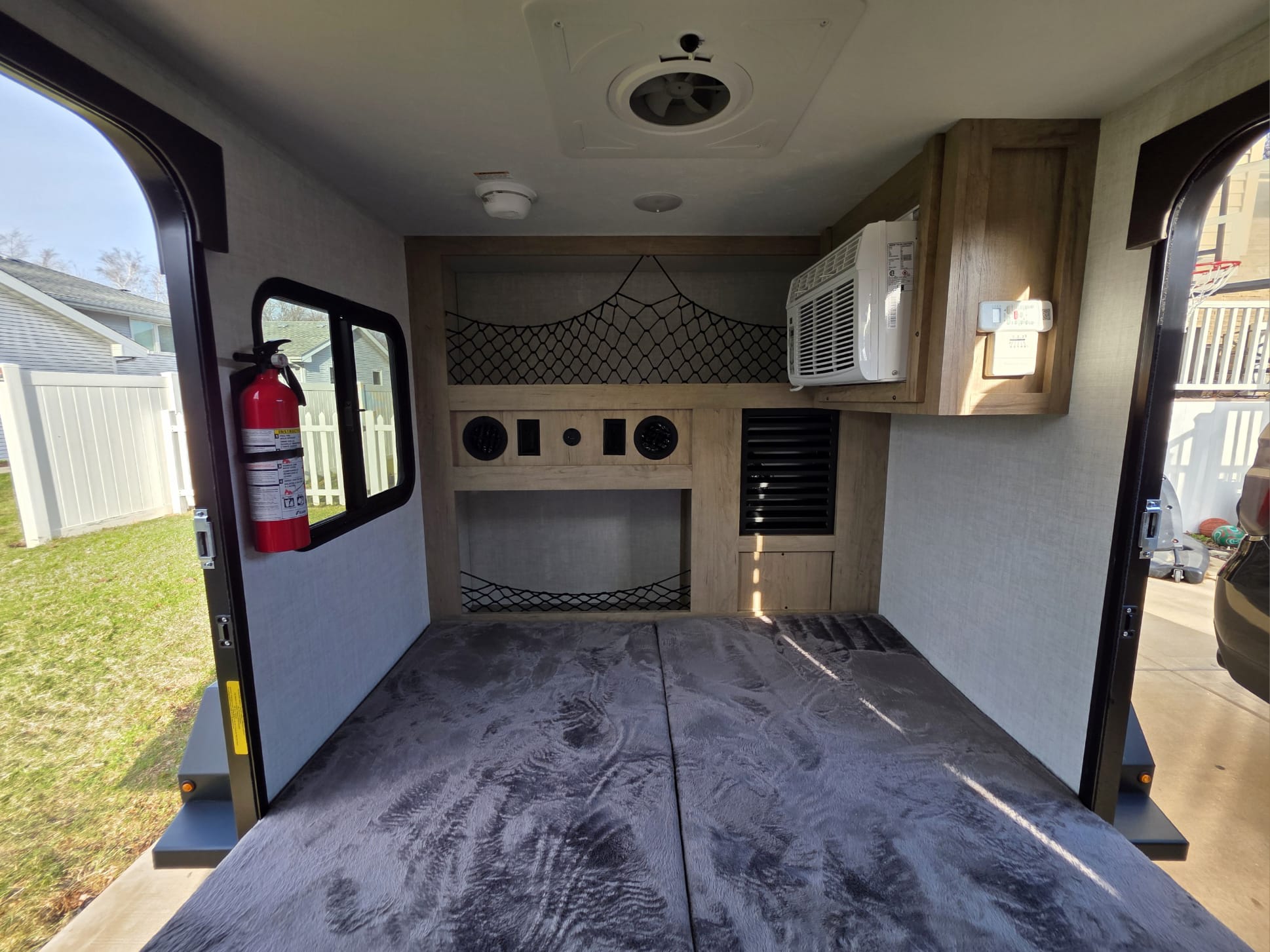 Inside an rv rental, featuring a bed, AC, overhead storage net, and fire extinguisher. Rear door open to outside.. Ember E Series Spark LE 2026
