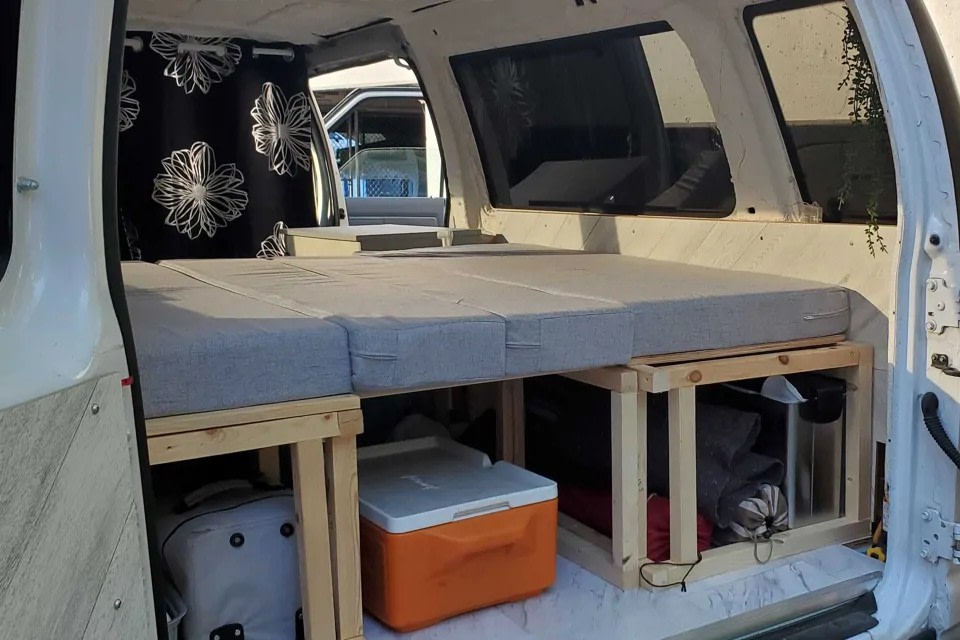 Functional RV rental interior: a raised bed with ample storage for gear & cooler, ideal for van life.. Ford Econoline Club Wagon 2011