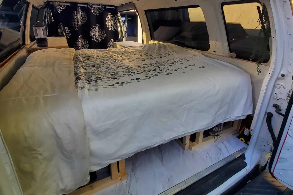 RV rental camper van interior featuring a comfortable, built-in bed with white and patterned bedding, plus storage space below.. Ford Econoline Club Wagon 2011