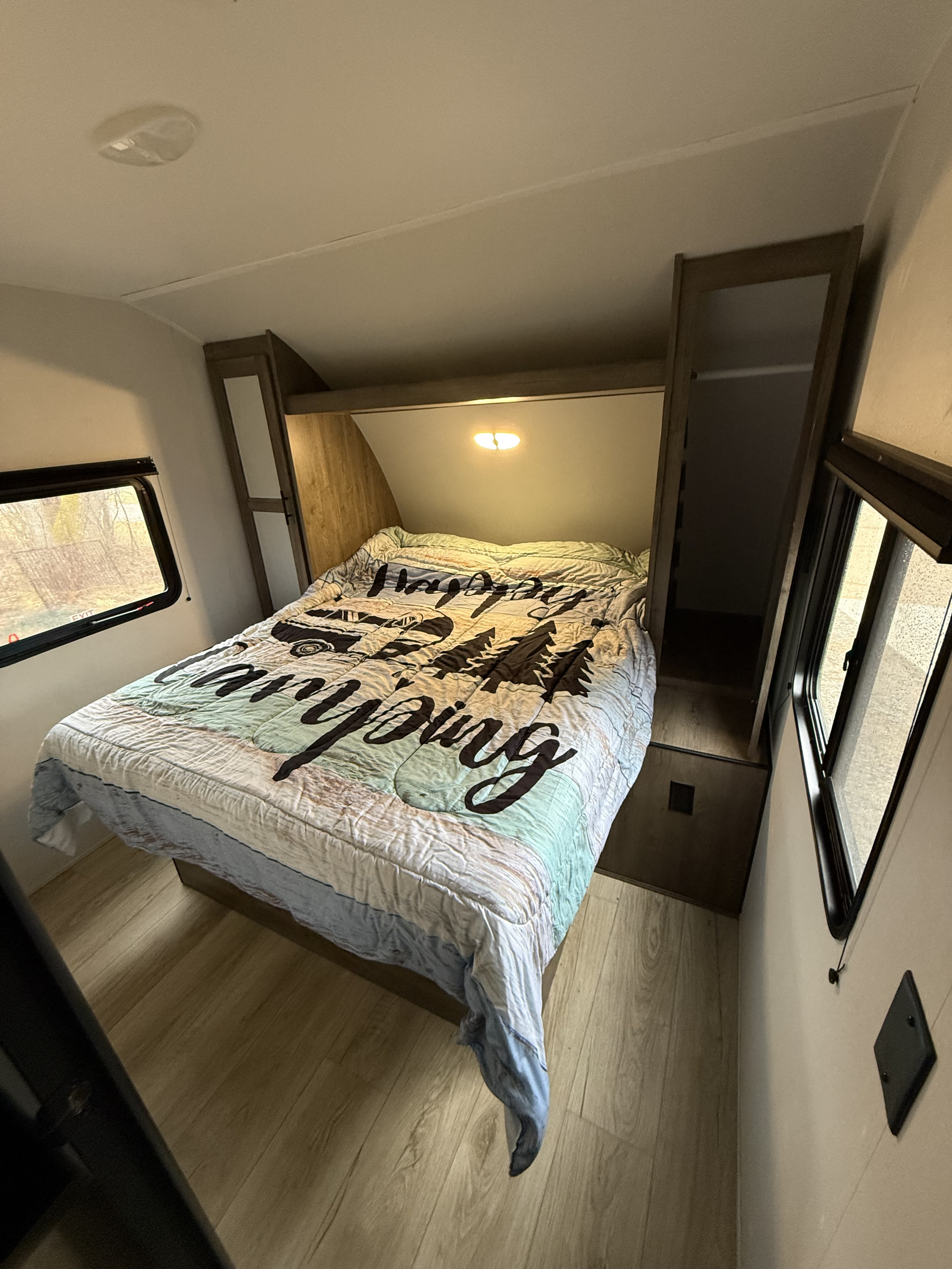 Cozy RV rental bedroom with a "Happy Camping" bed, built-in storage, and bright windows for your adventure.. Heartland RVs Pioneer 2024