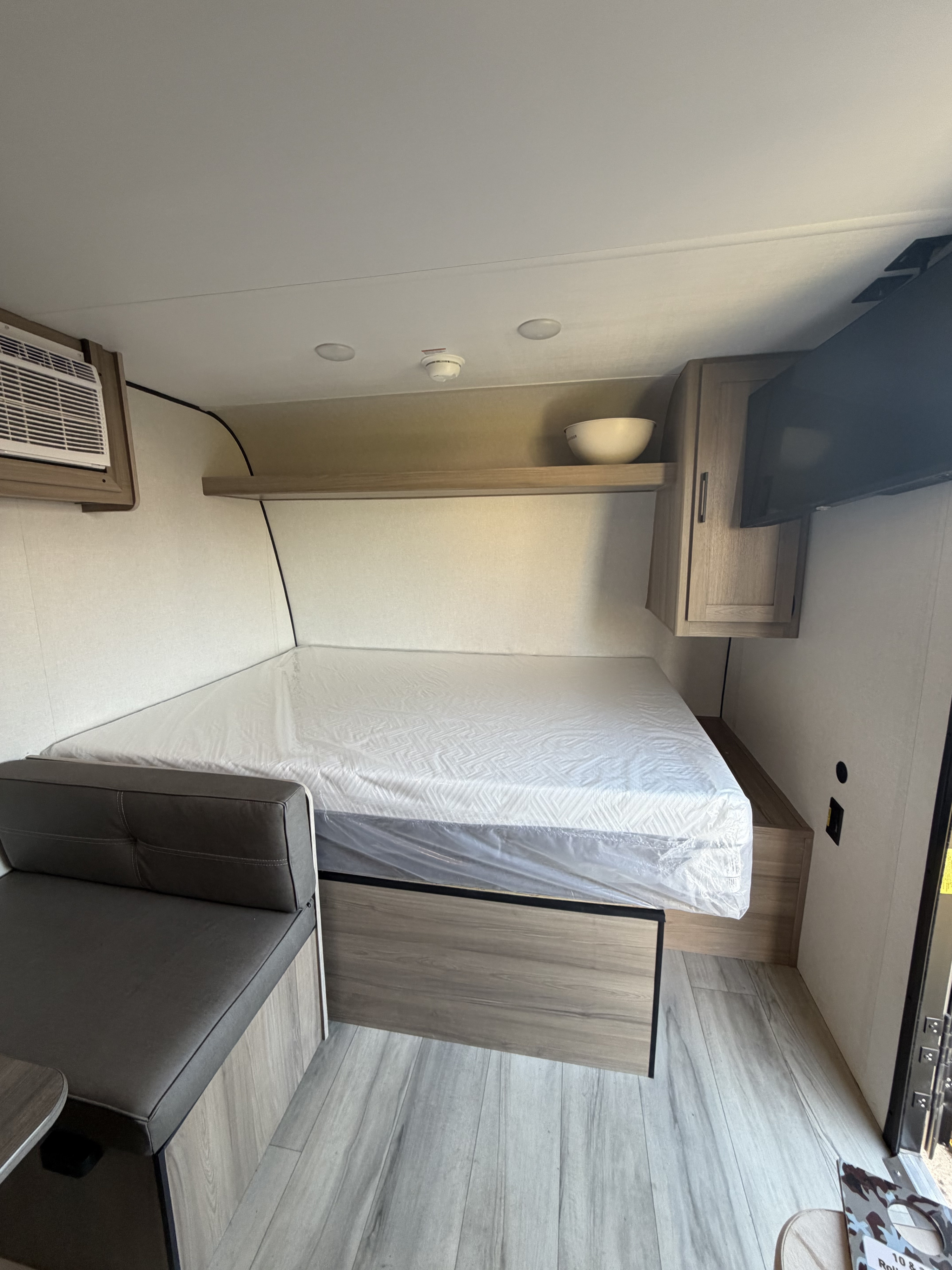 RV rental interior: Compact sleeping and living space in a modern camper with a wrapped bed, bench, and AC unit.. Keystone RV Coleman 2025