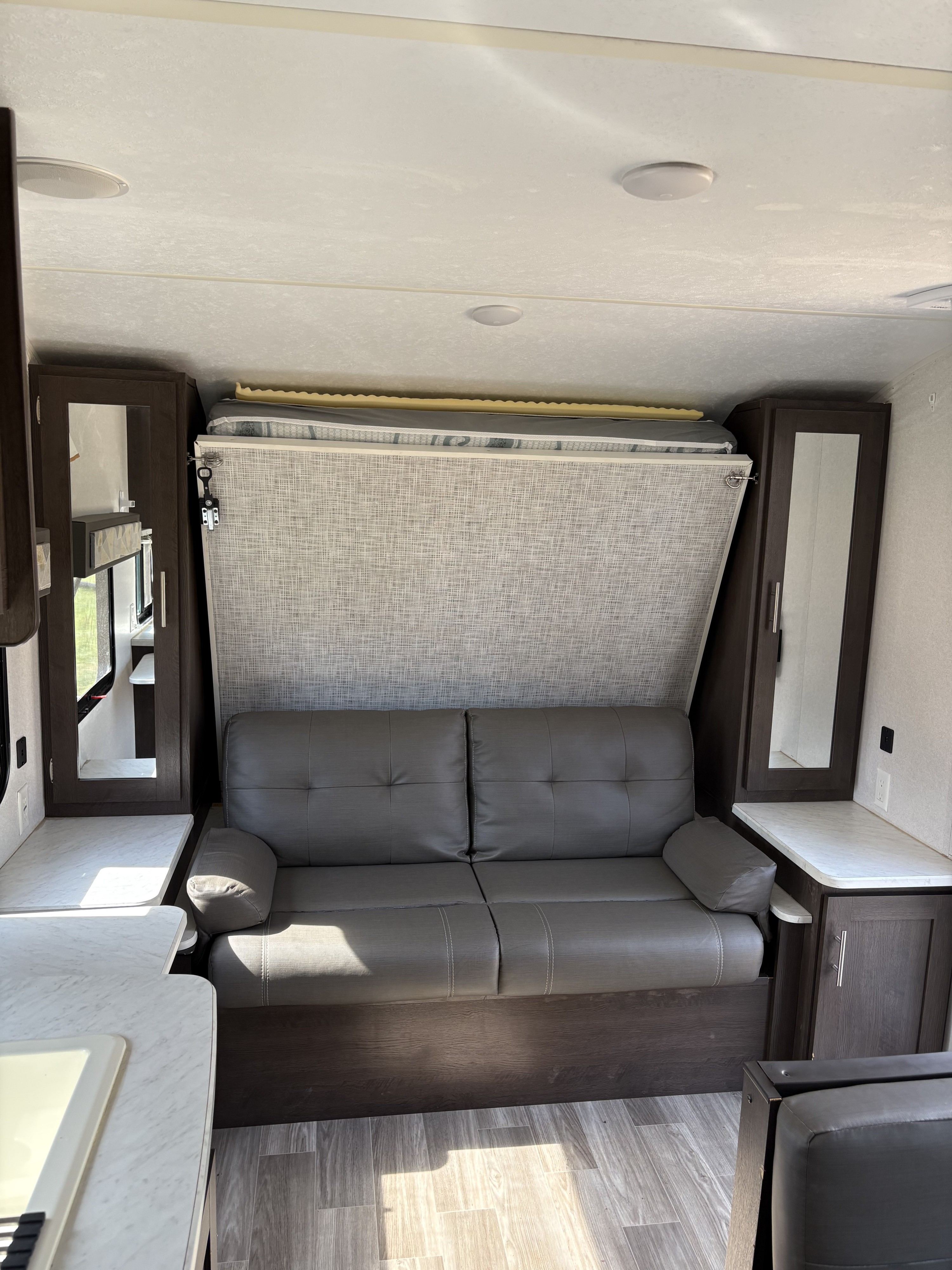 Inside an rv rental: gray sofa below a neatly folded murphy bed, flanked by dark cabinets and counters.. Forest River Salem Cruise Lite 2019