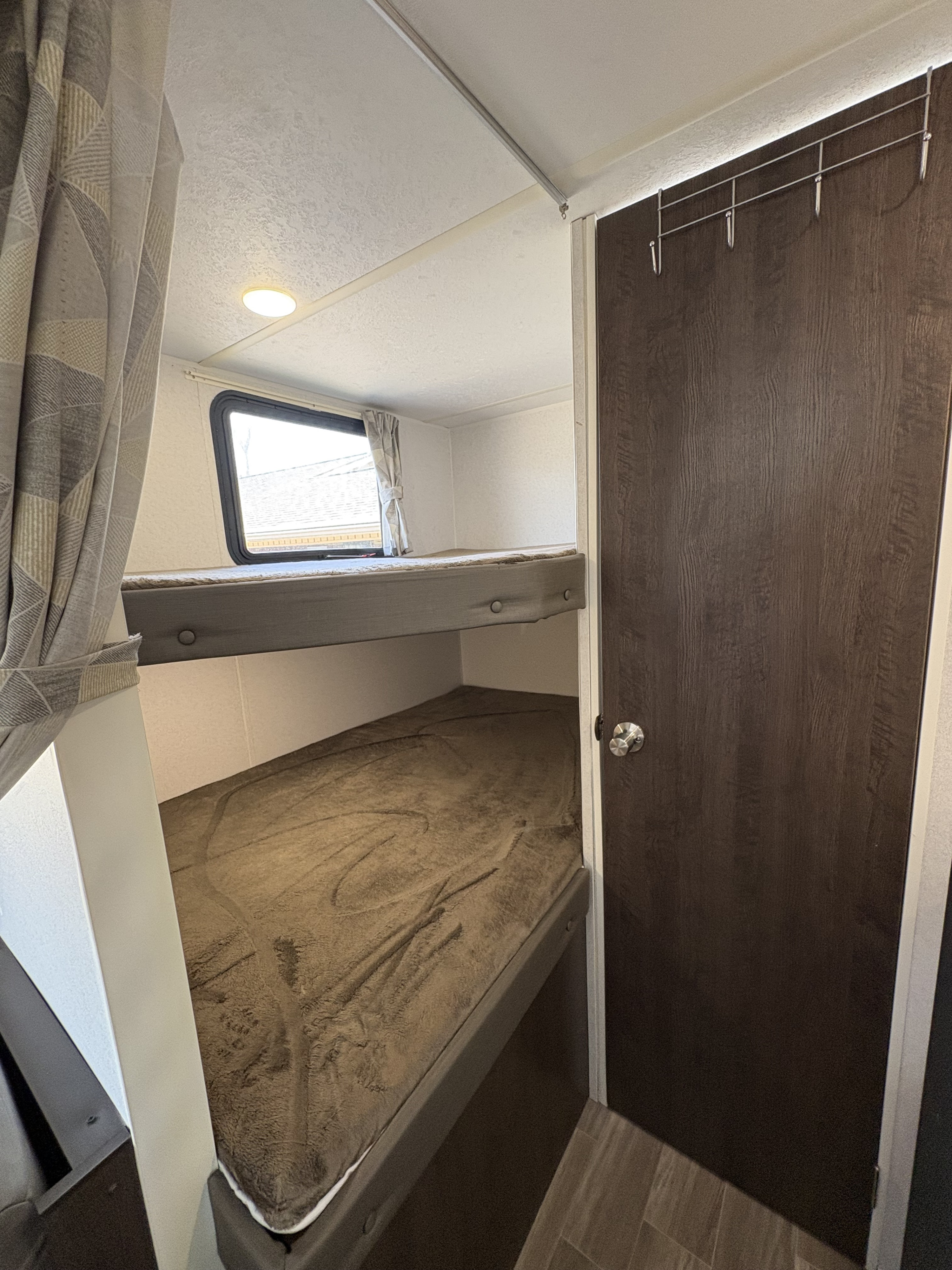 Cozy RV rental interior featuring stacked bunk beds with a window, and a dark wood door with an over-door hook rack.. Forest River Salem Cruise Lite 2019