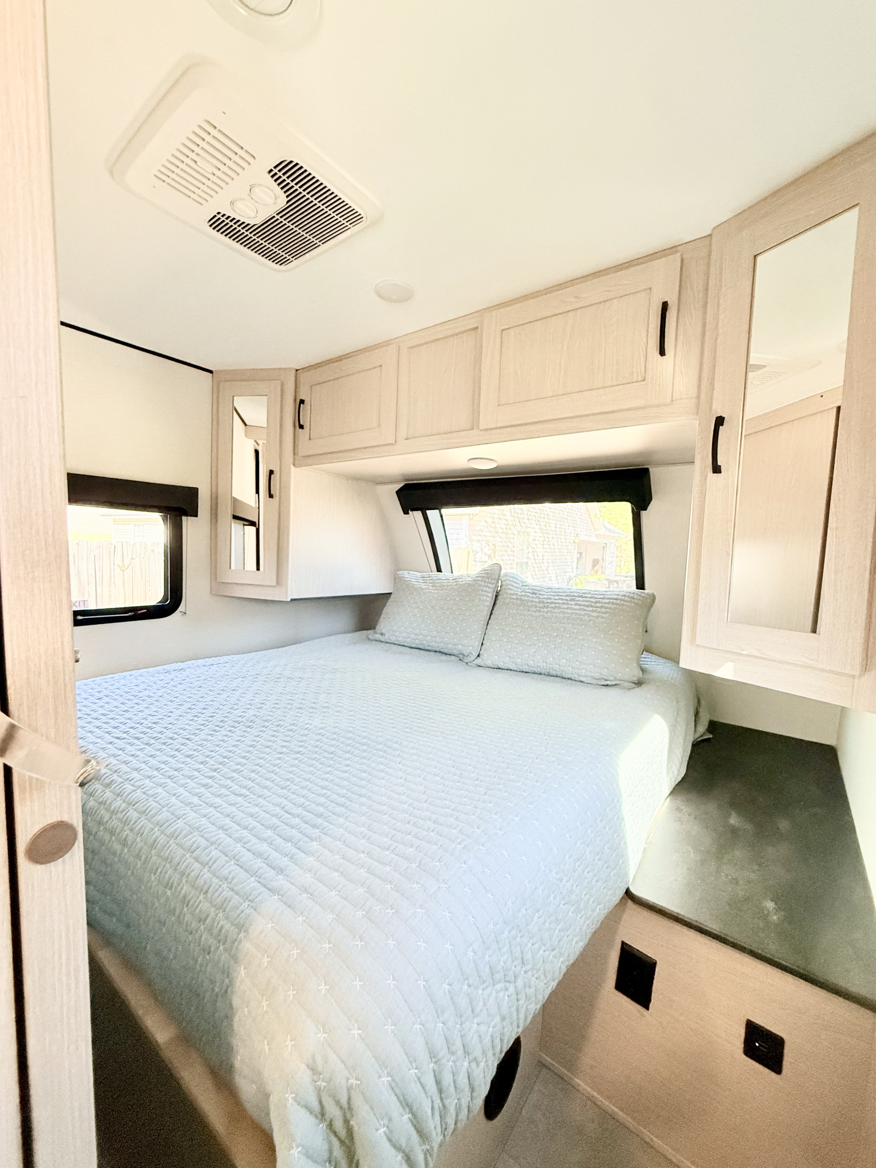 Modern RV rental bedroom with light wood cabinets, a comfy quilted bed, window, and ceiling AC unit.. Coachmen Apex 2022